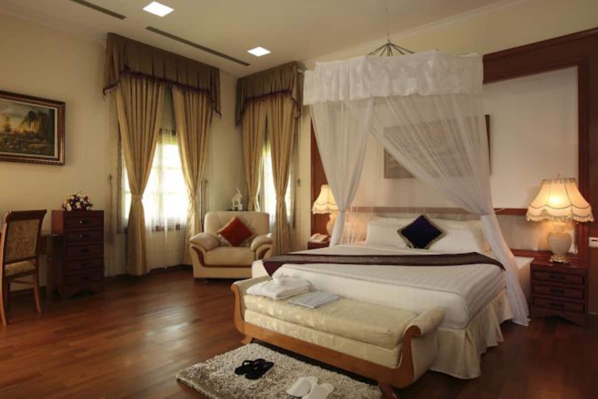 Quarto com cama de dossel, escrivaninha com computador, cadeira e mesa de cabeceira com abajur.
