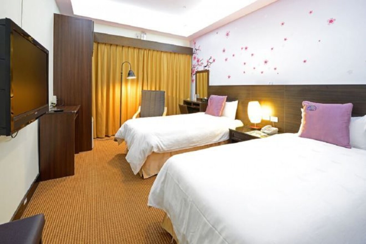 A hotel room with two beds, a TV, a desk, and a wall with floral decorations.