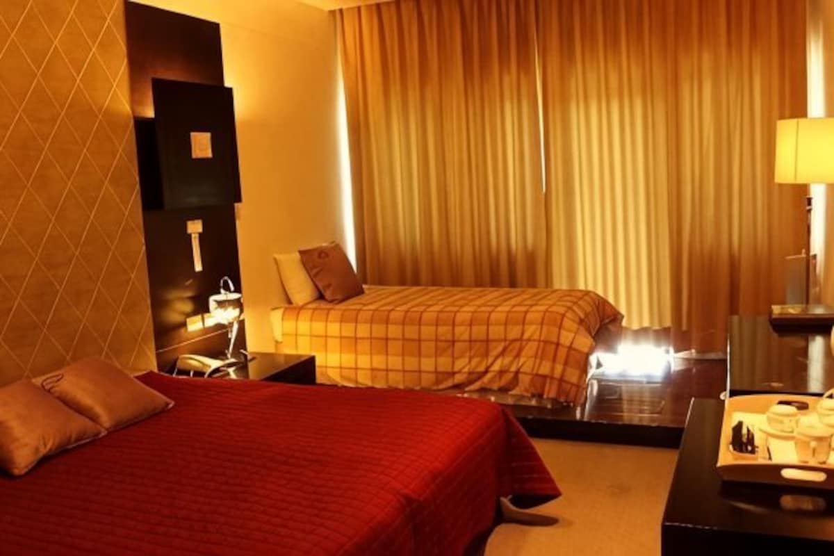A hotel room with two beds, a desk, a chair, a TV, and a window with curtains.