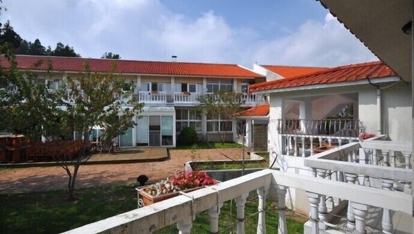 A hotel with a red-tiled roof, a covered outdoor area with a white railing, and a small garden with a tree and flower arrangement. - Cingjing Guest House (Ren'ai)