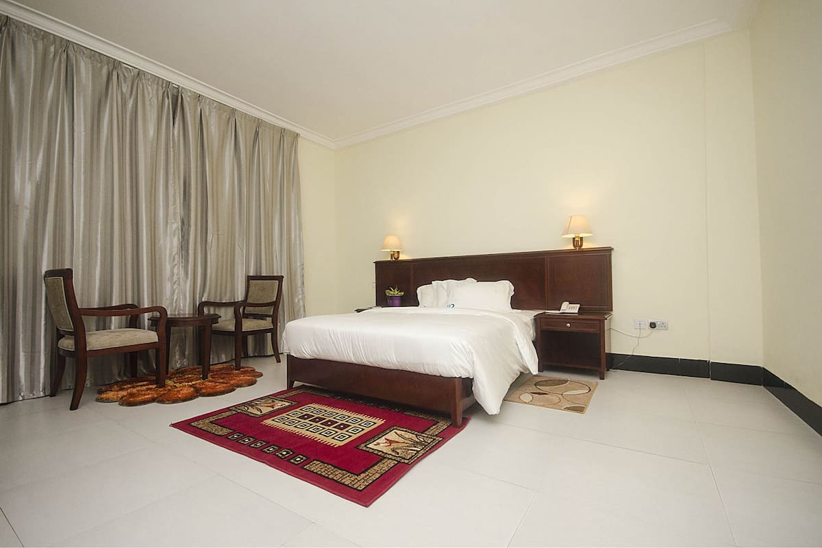 A hotel room with a large bed, two bedside tables with lamps, a chair, a small table, and a decorative rug.