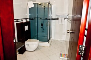 A bathroom with a glass-enclosed shower, a toilet, and a sink. - Birdrock Hotel (Anomabo)