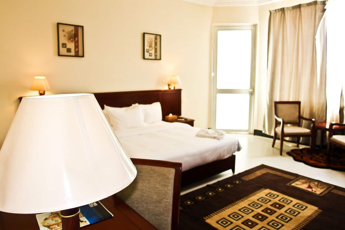 A hotel room with a bed, bedside lamps, a chair, a table, and a window with curtains.
