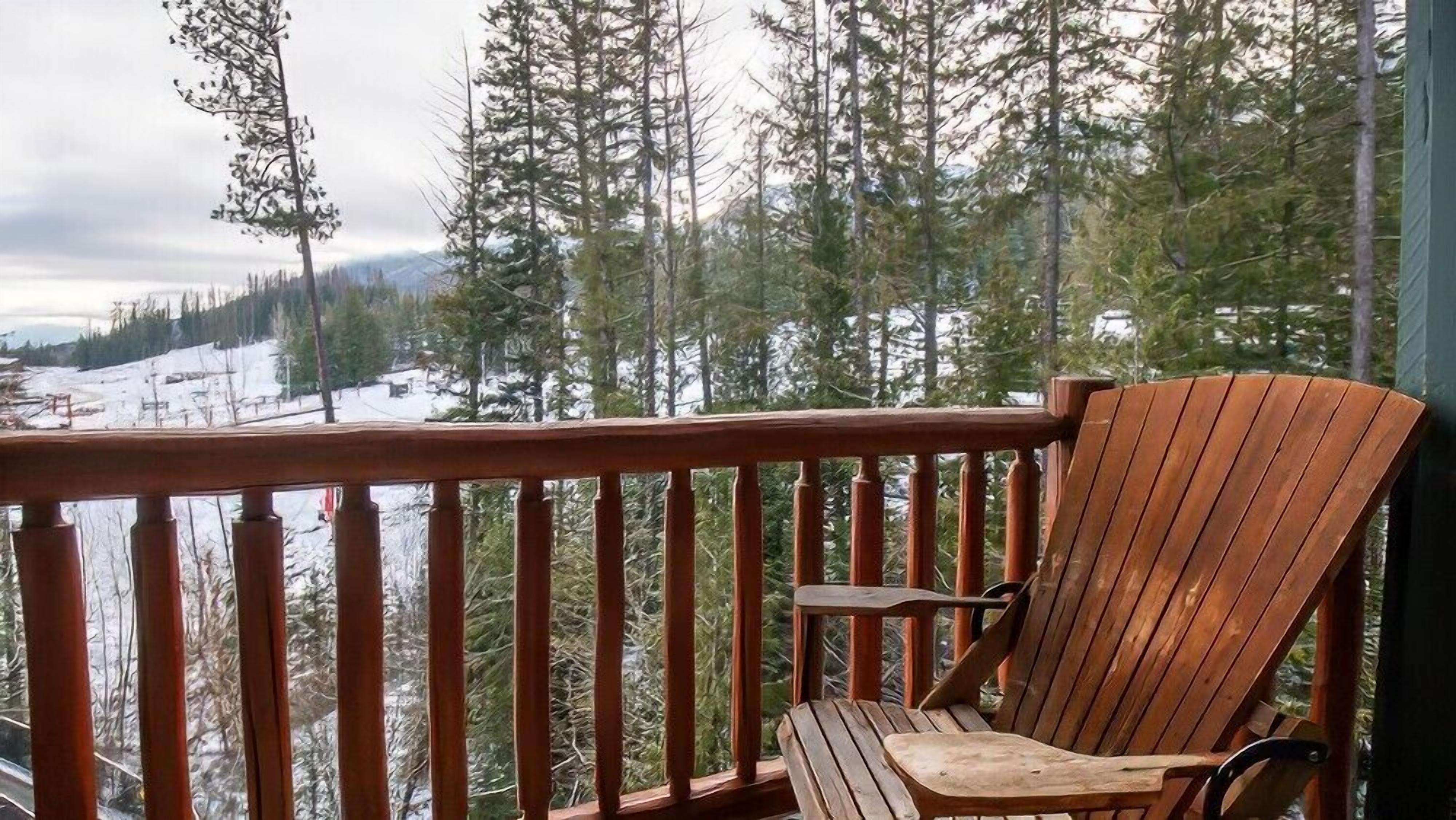 Une terrasse en bois avec une chaise en bois, d’où l’on peut admirer un paysage enneigé avec des arbres et des montagnes en arrière-plan.