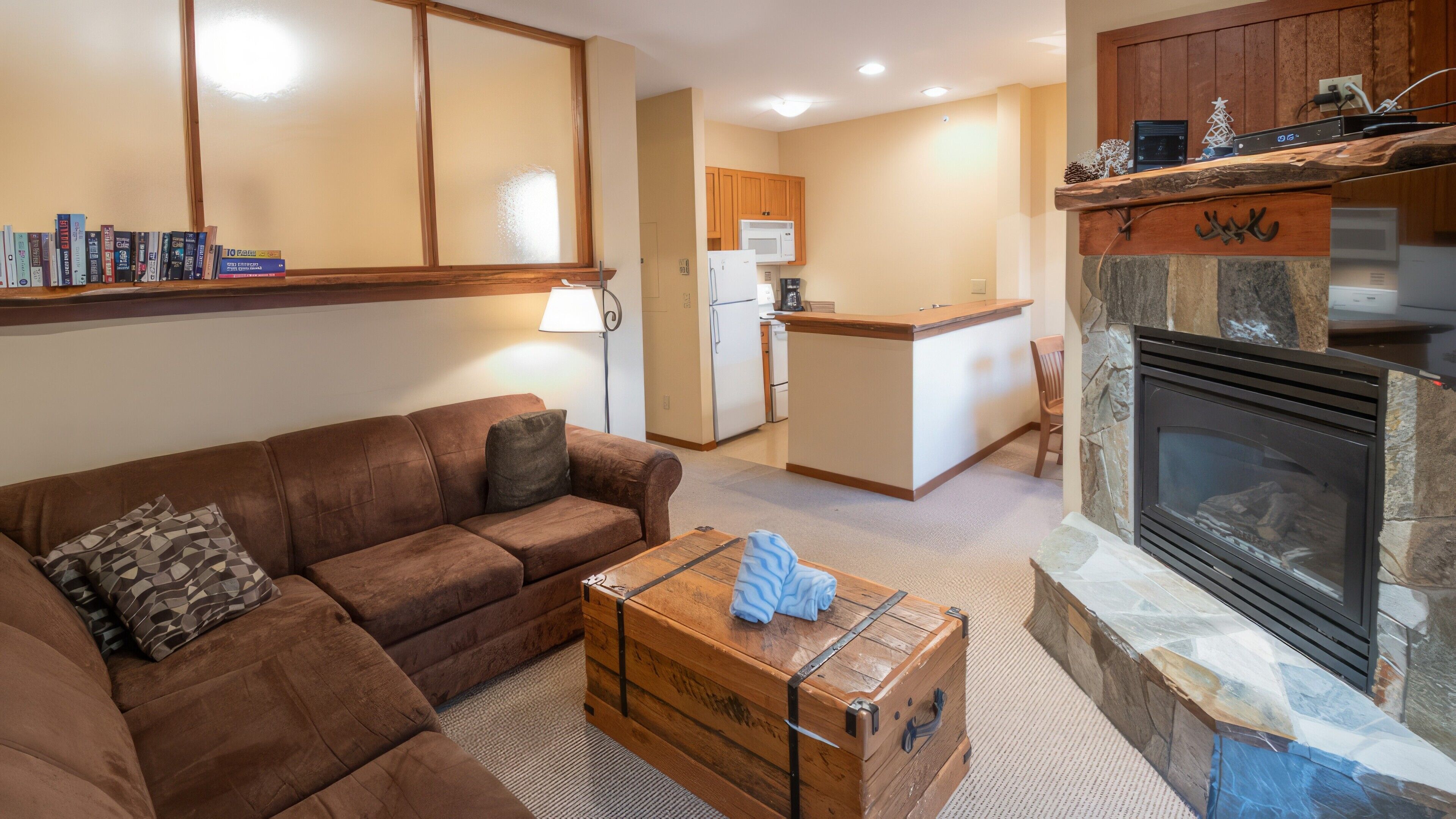 A living room with a brown sofa, a wooden chest, and a stone fireplace.