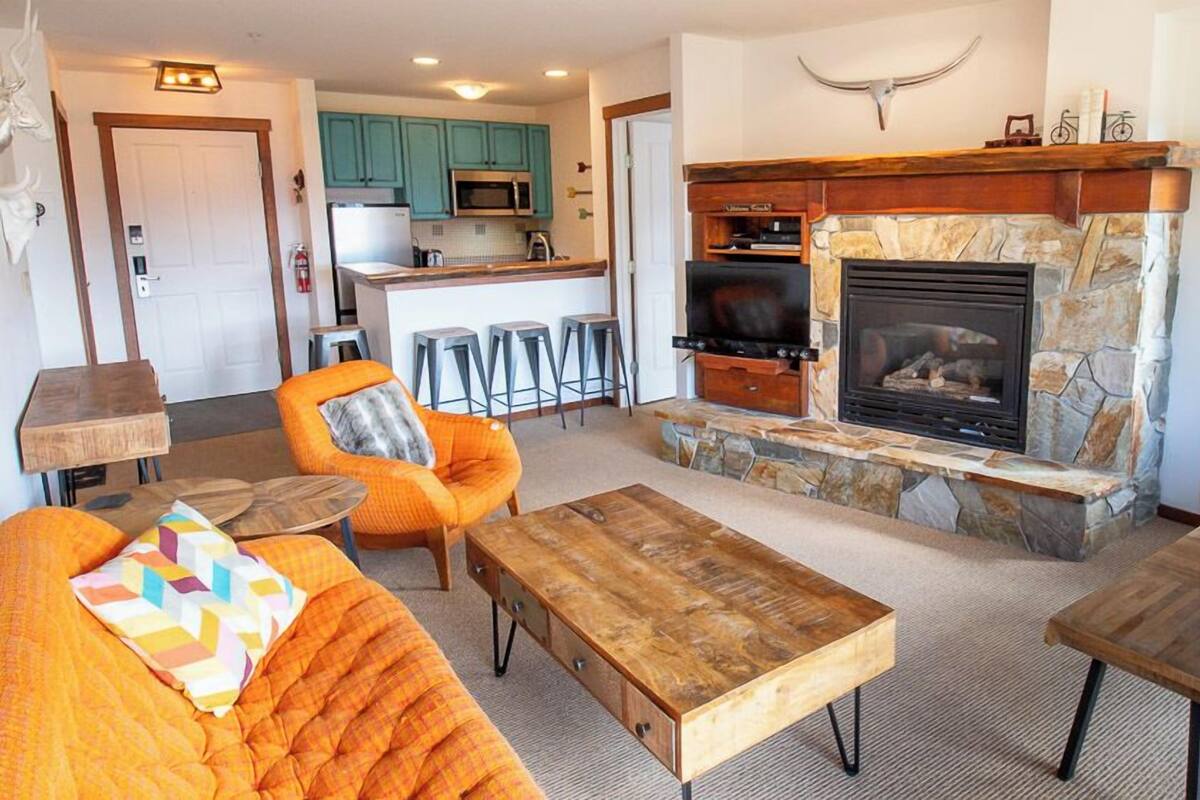 Ein gemütliches Wohnzimmer mit Kamin aus Stein, einer bequemen orangefarbenen Couch und einem Holztisch.