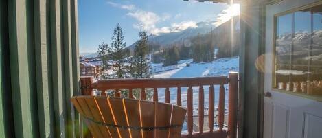 A wooden chair on a balcony with a view of a snowy landscape and mountains.