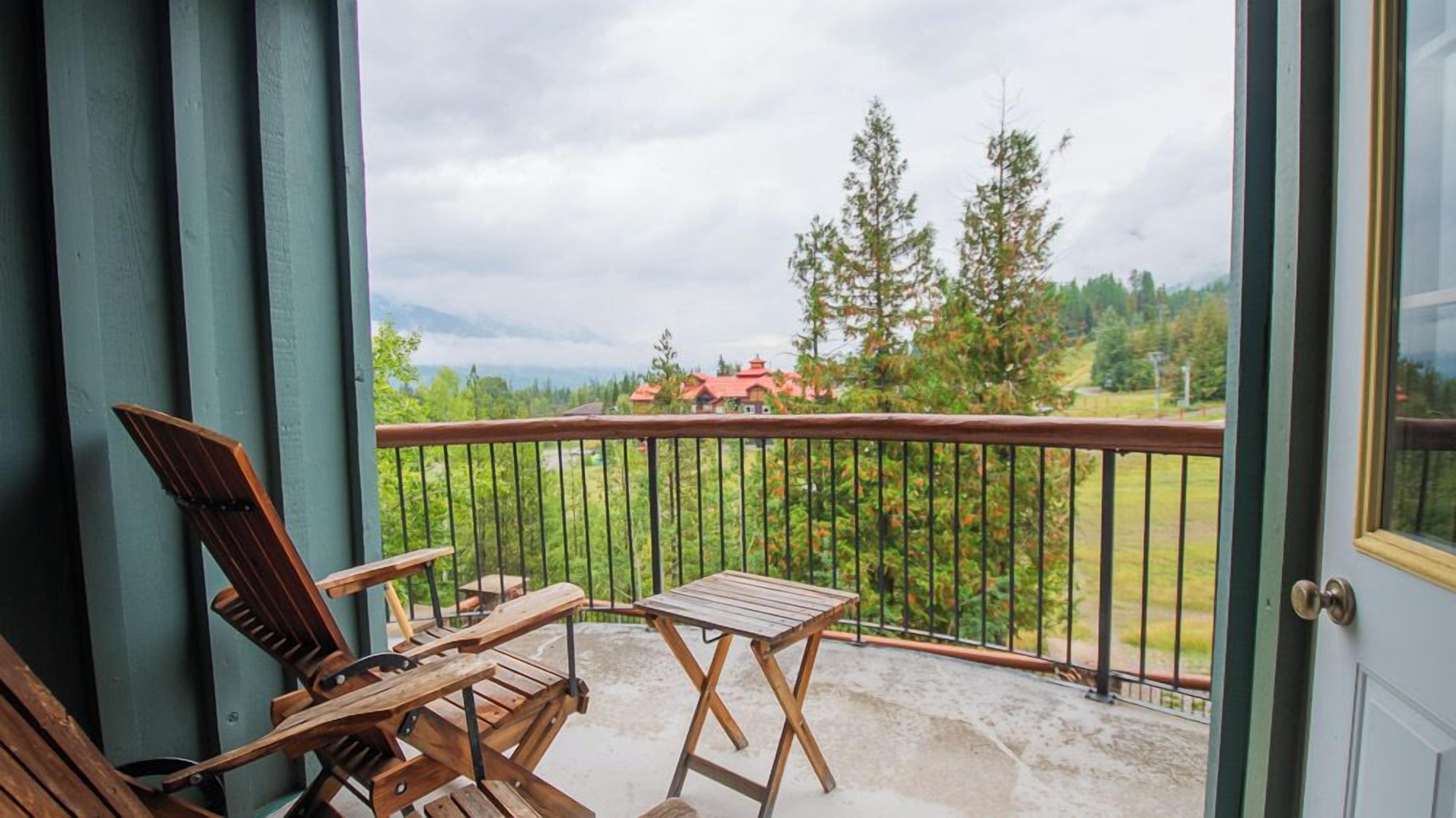 A balcony with a view of a red-roofed house, surrounded by trees and a cloudy sky.