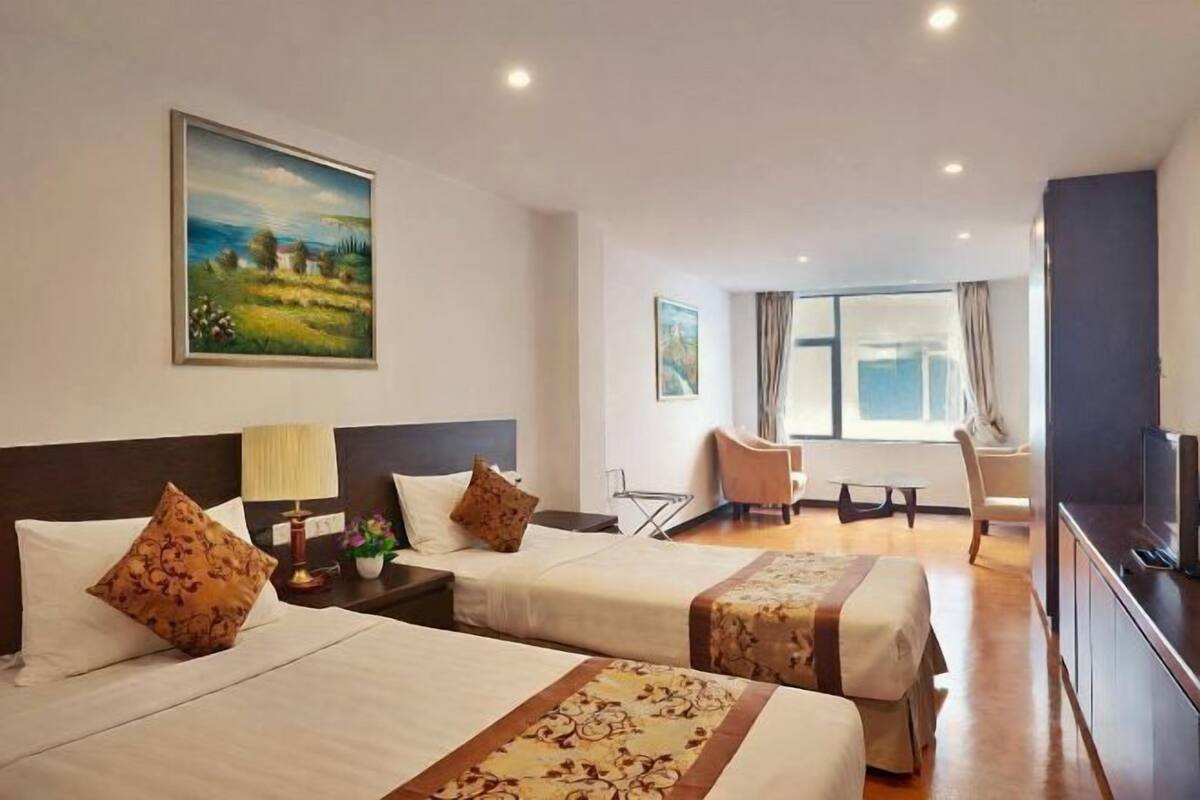 A hotel room with two beds, a desk, a chair, a television, and a painting on the wall.