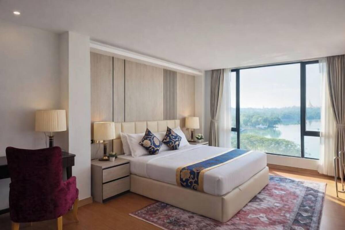A hotel room with a large bed, nightstands, a desk, a chair, and a view of the outdoors.