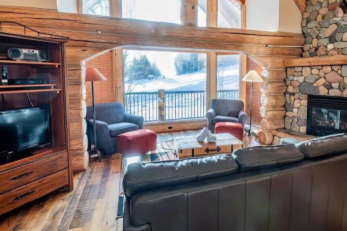 Ein gemütliches Wohnzimmer mit Kamin aus Stein, einer Ledersofa und einem Fernseher auf einem Holzboden.