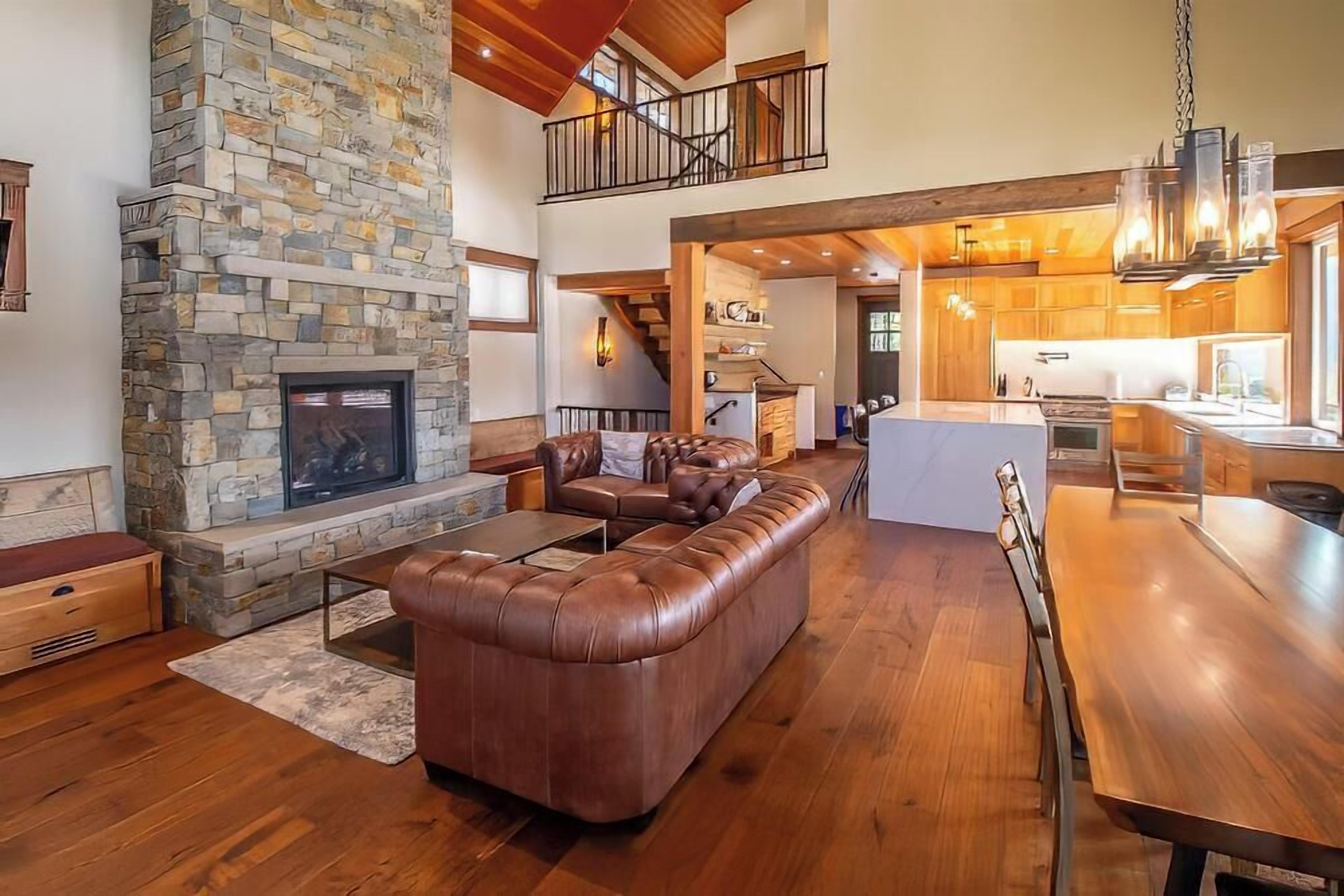 A spacious living area with a stone fireplace, leather sectional sofa, and a wooden dining table.