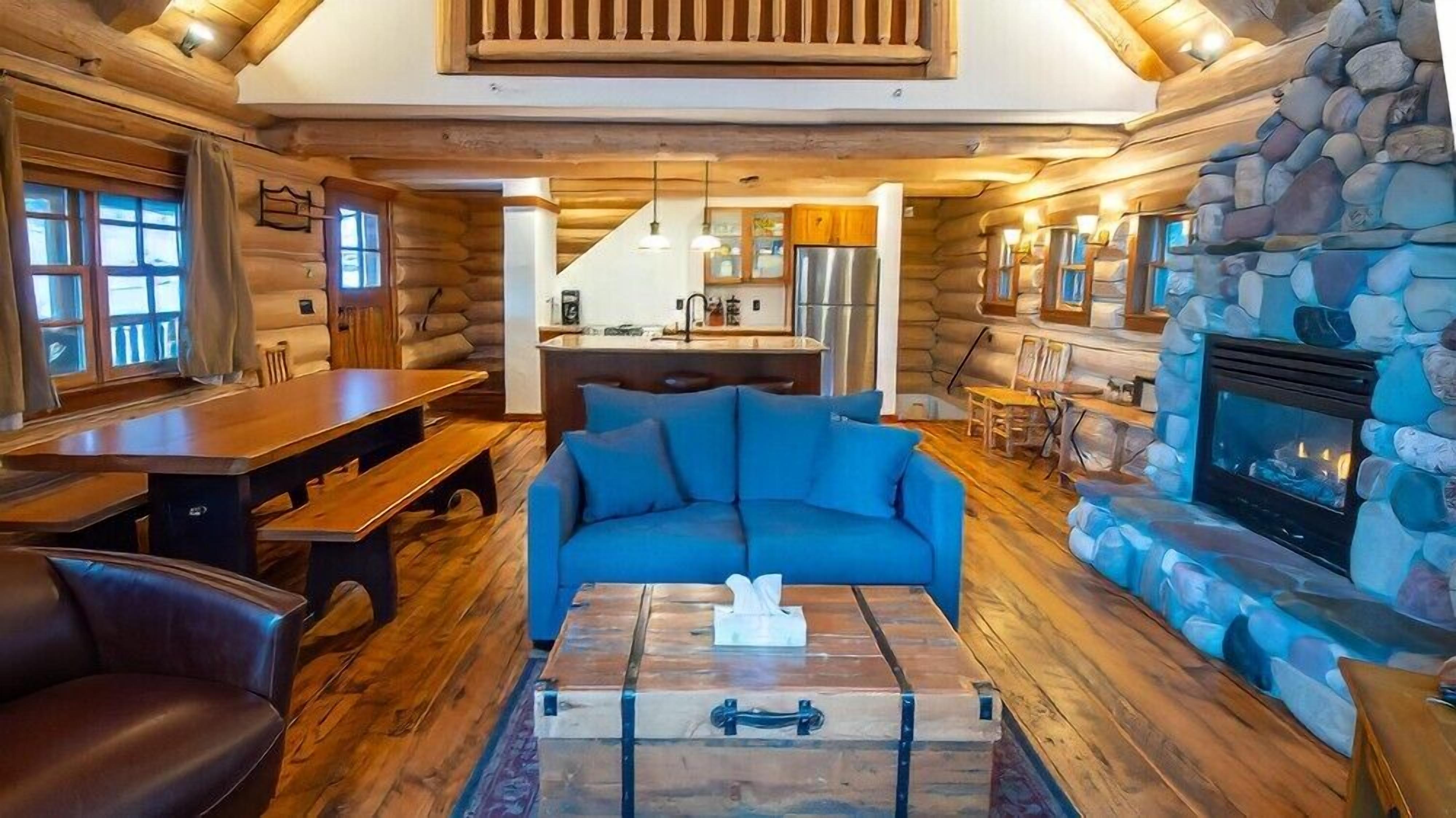 A log cabin interior with a dining area, a sofa, a fireplace, and a kitchen.