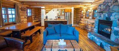 A log cabin interior with a dining area, a sofa, a fireplace, and a kitchen.