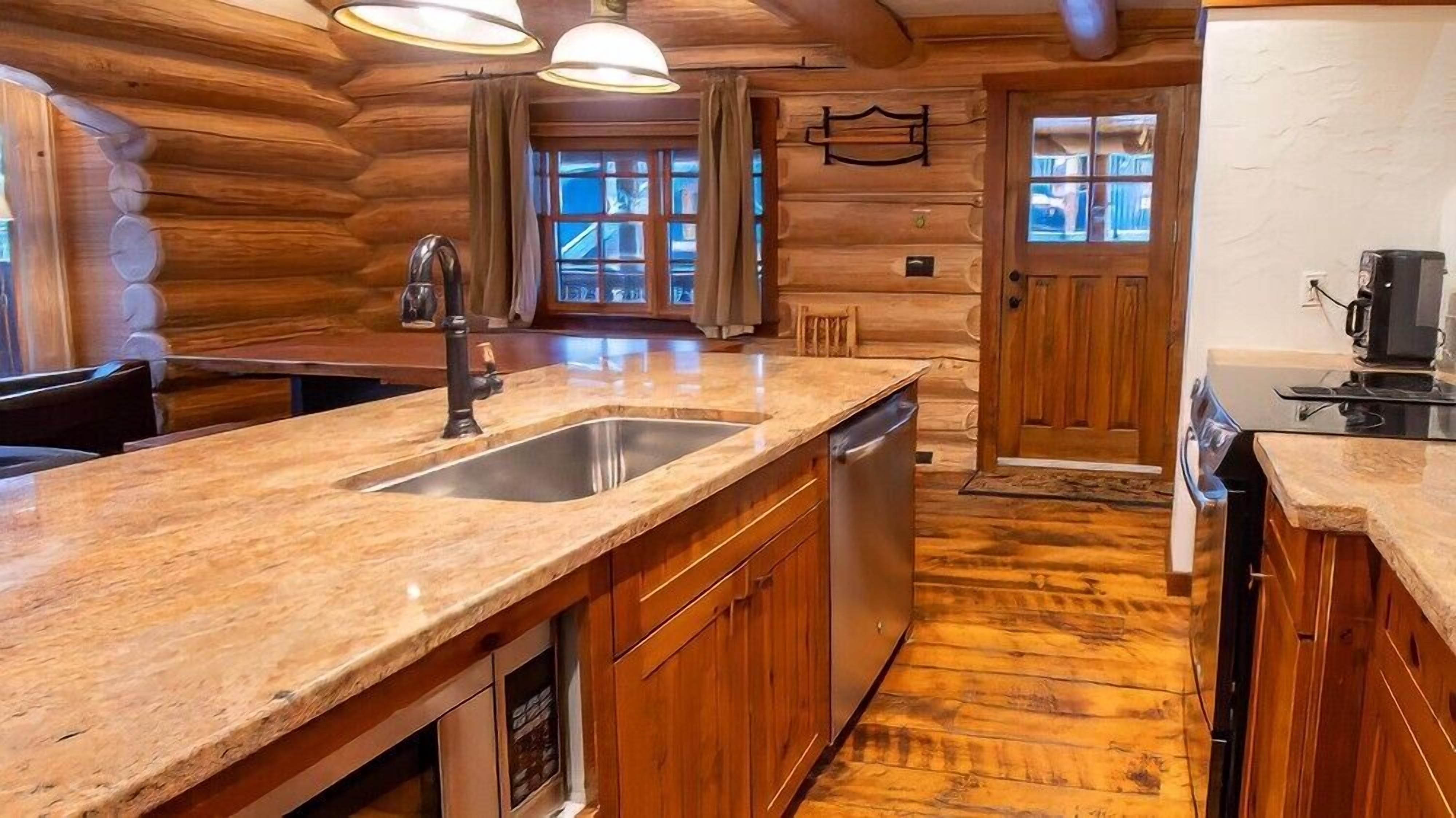 A log cabin kitchen with a granite countertop, stainless steel sink, and wooden cabinets.