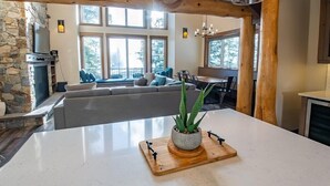 Eine moderne Küche mit Wandverkleidung aus Stein, einem eingebauten Grill und einem großen Fenster mit Blick auf einen Wohnbereich mit grauem Sofa und blauen Kissen.