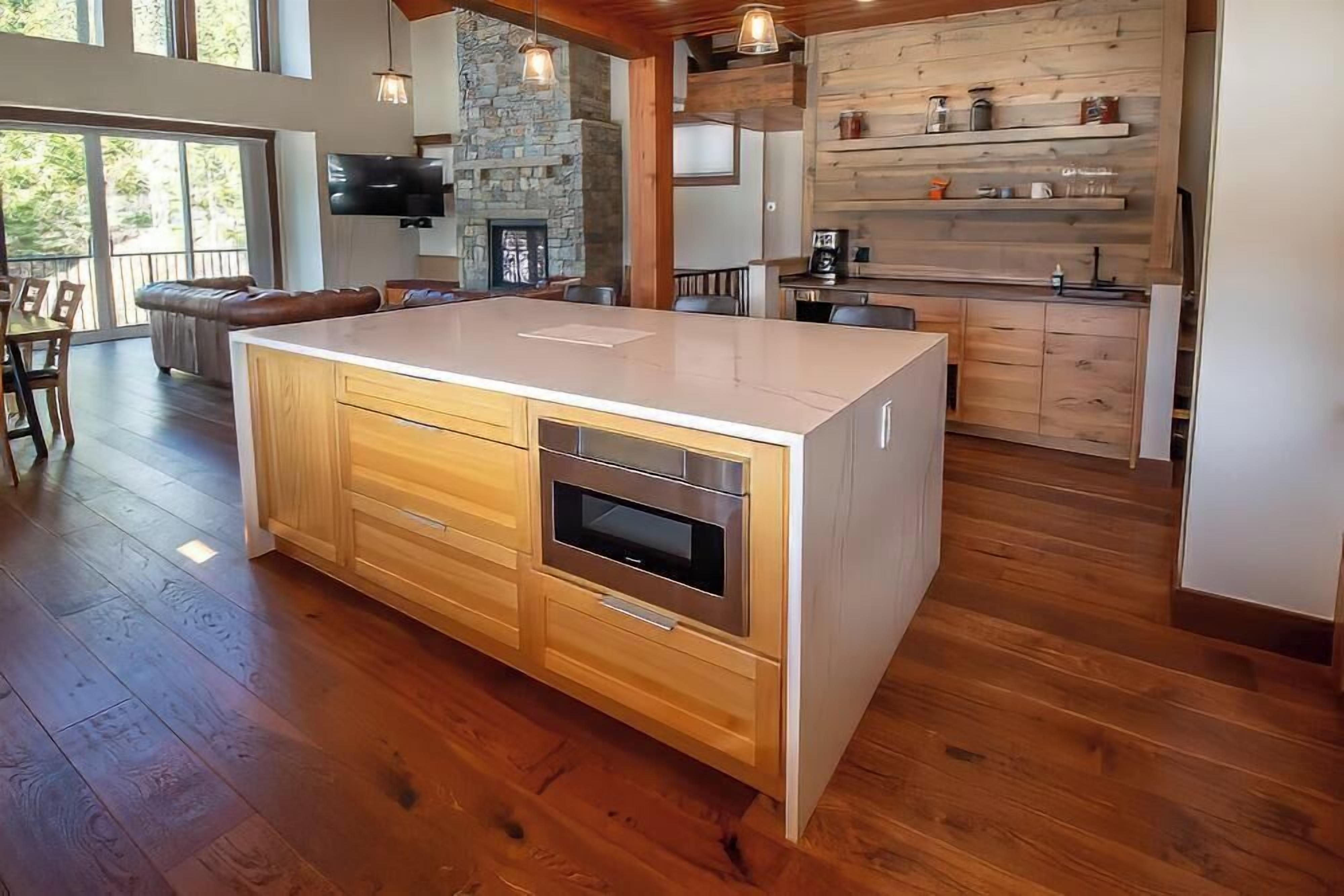 A spacious kitchen with a large island, wooden cabinets, and a stone fireplace.