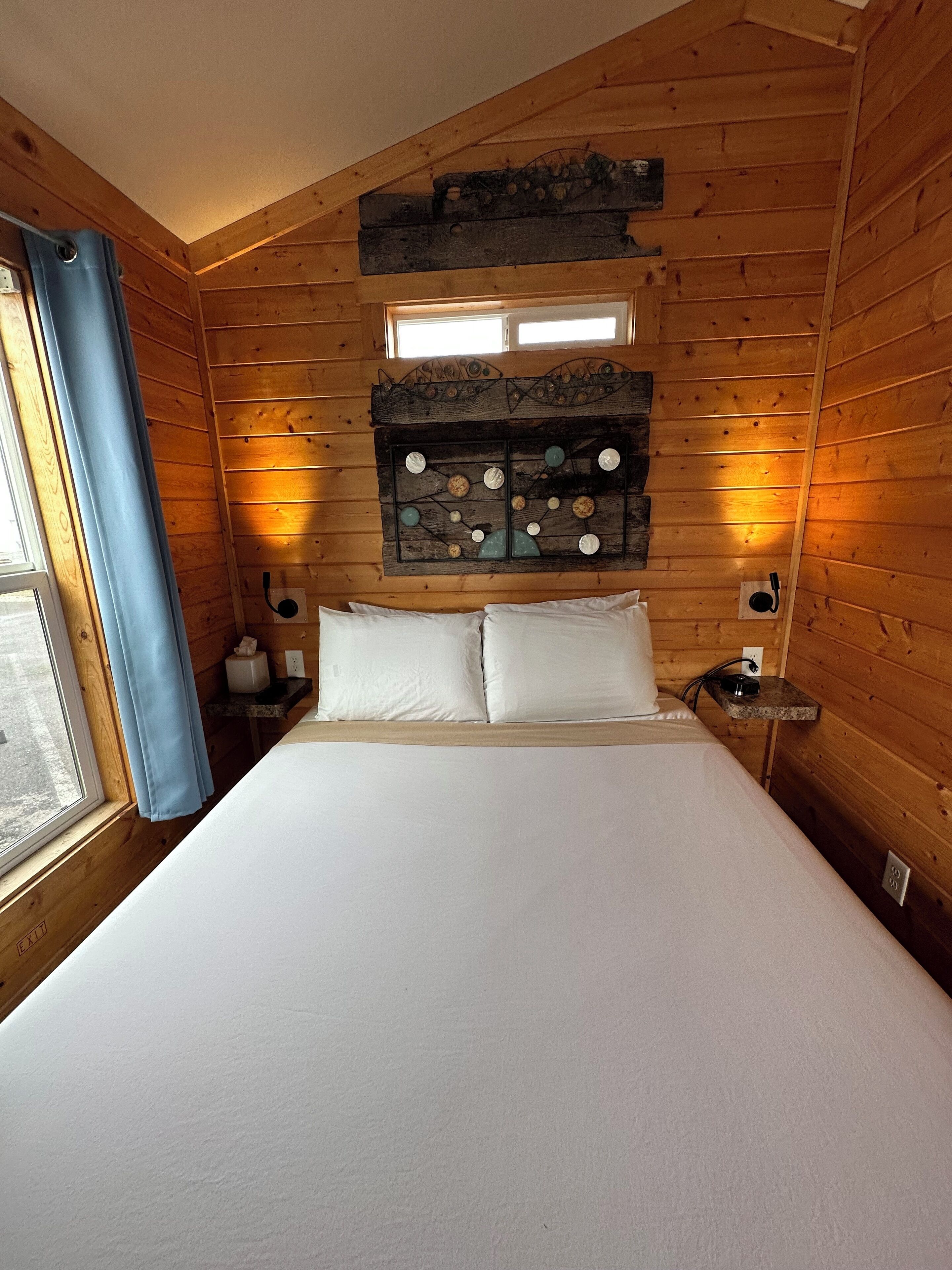 Un dormitorio de cabaña de madera con cama, un adorno en la pared y una ventana con cortinas.