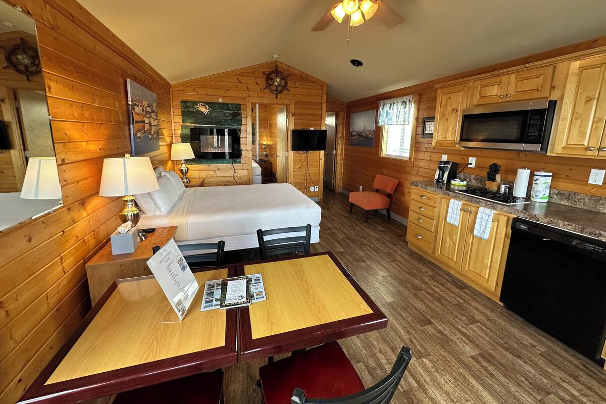 A cozy cabin-style room with a bed, a dining table, and a kitchen area.