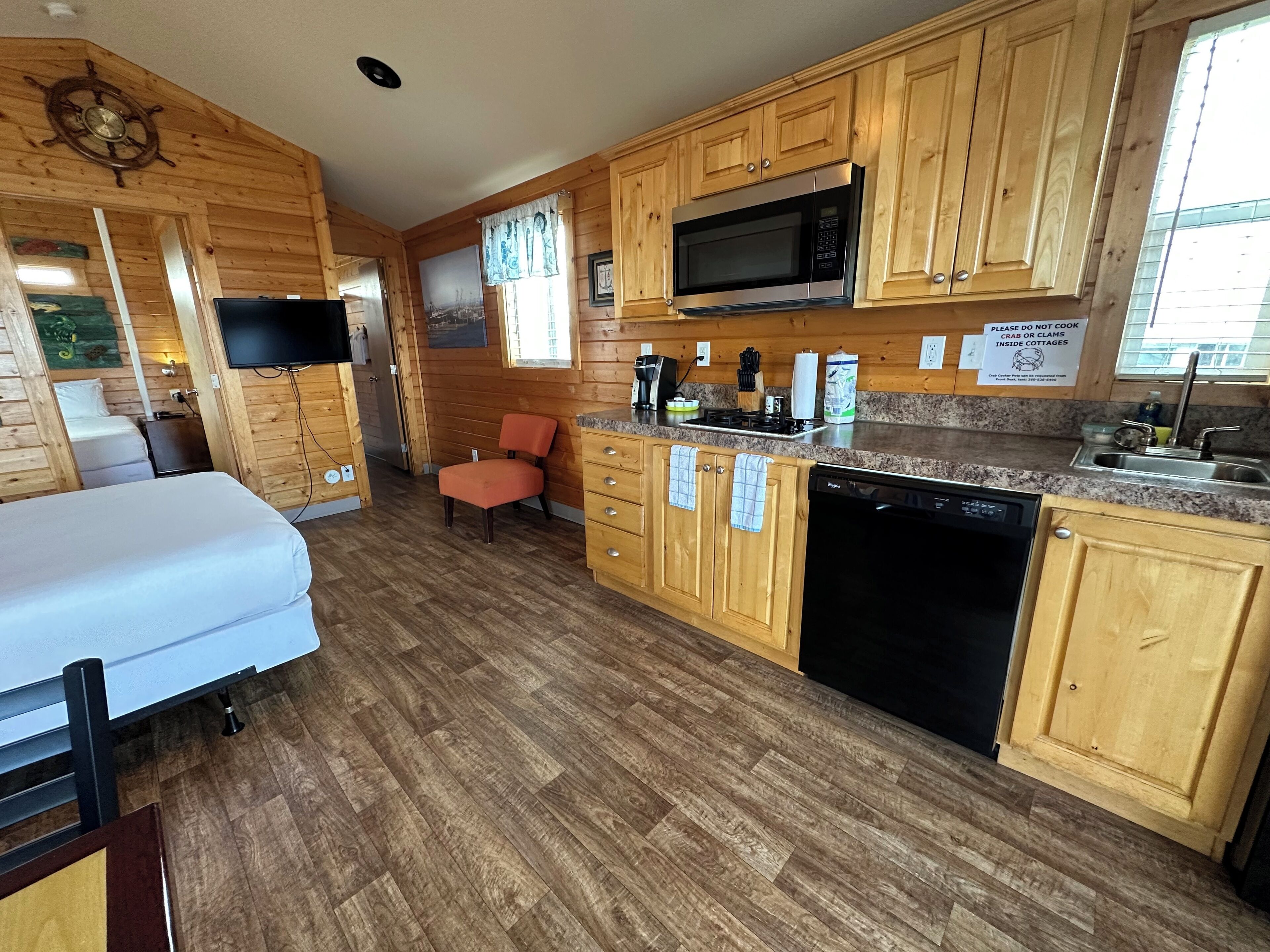 A compact kitchen with wooden cabinets, a microwave, a sink, and a dishwasher.