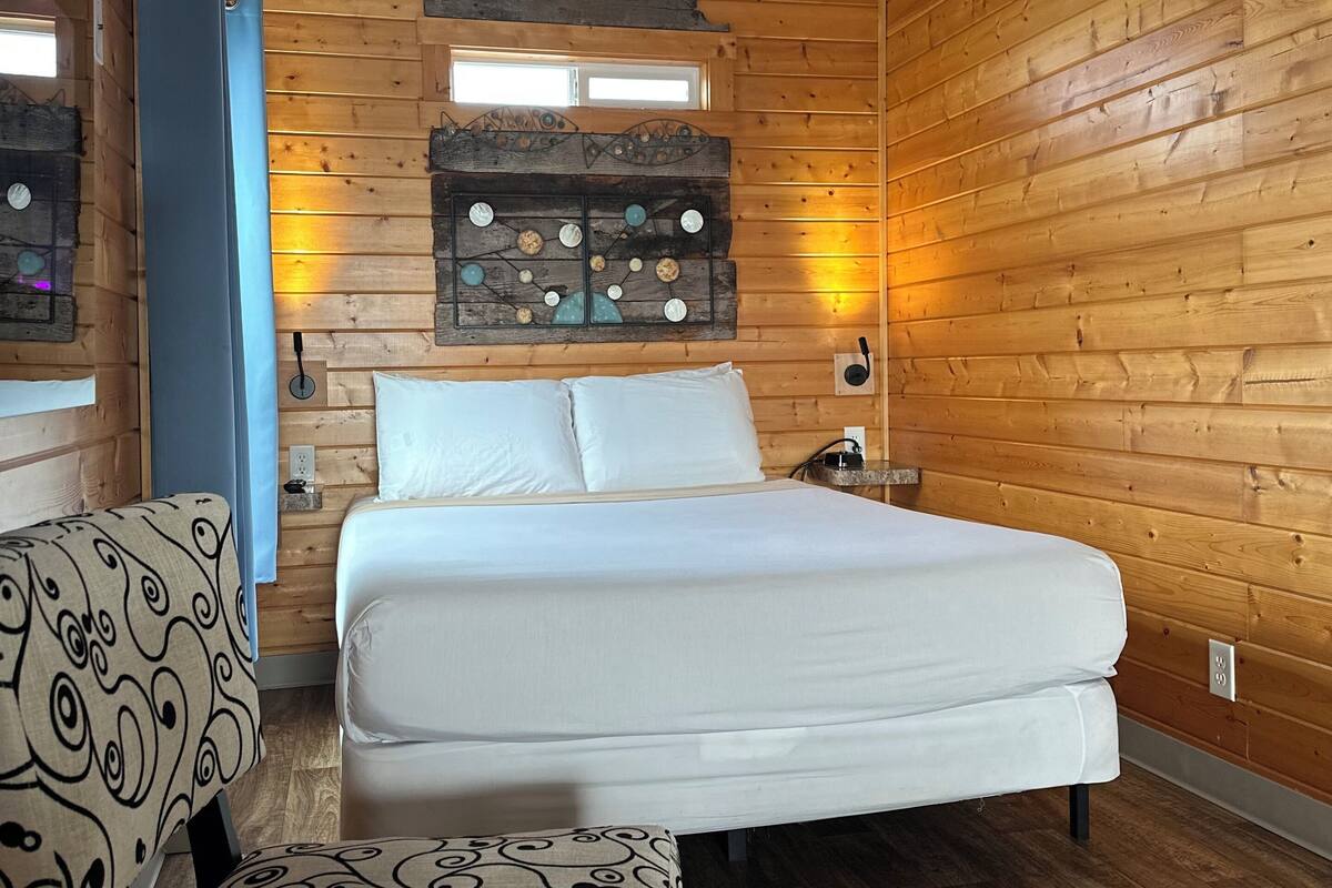 A wooden-paneled room with a bed, a chair, and a decorative wall piece.