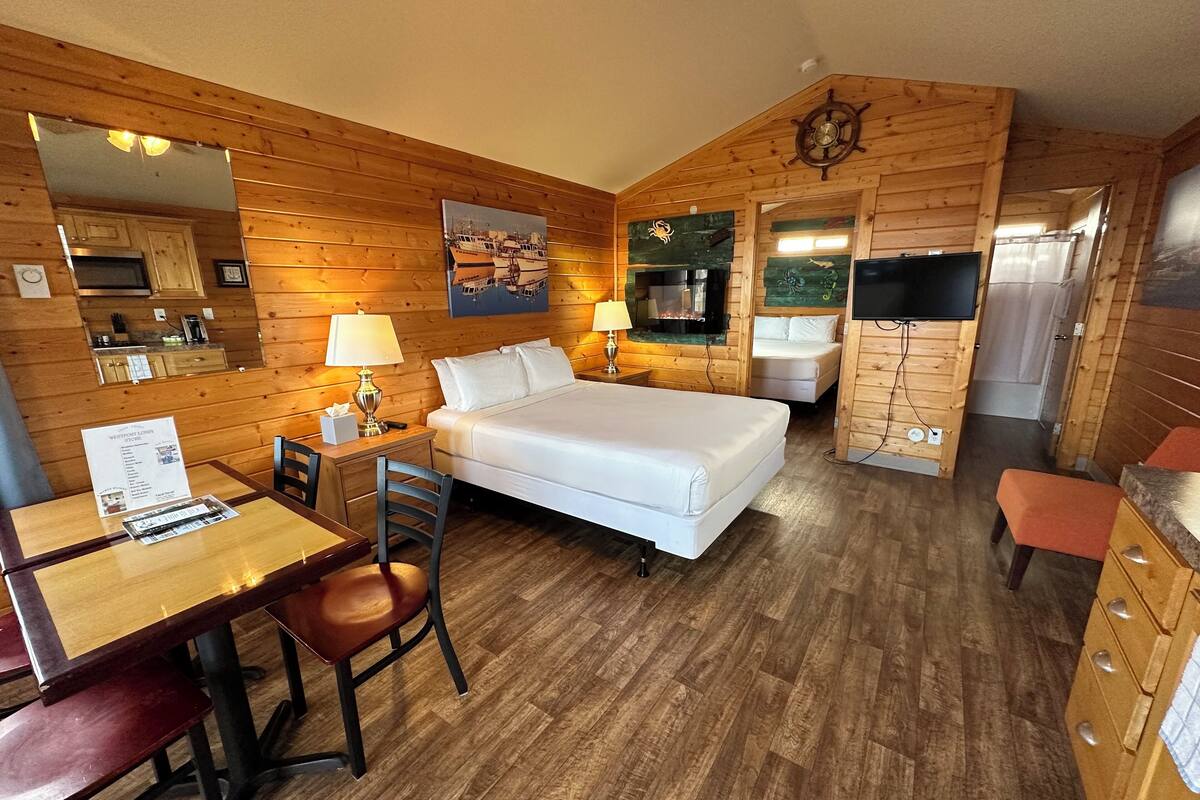 A cozy cabin-style room with a wooden interior, a bed, a desk with a chair, a television, and a fireplace.