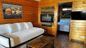 L’intérieur d’un chalet en bois, avec un canapé, une petite table, un téléviseur et un tableau représentant des bateaux.