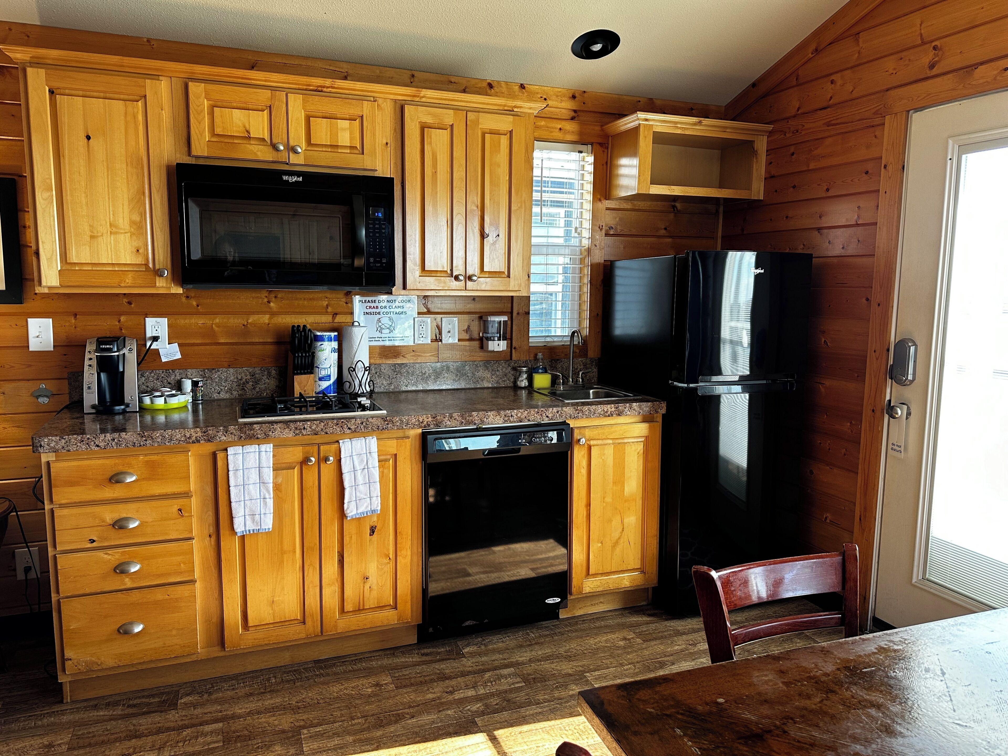 A wooden cabin-style kitchen with a microwave, stove, sink, and refrigerator.