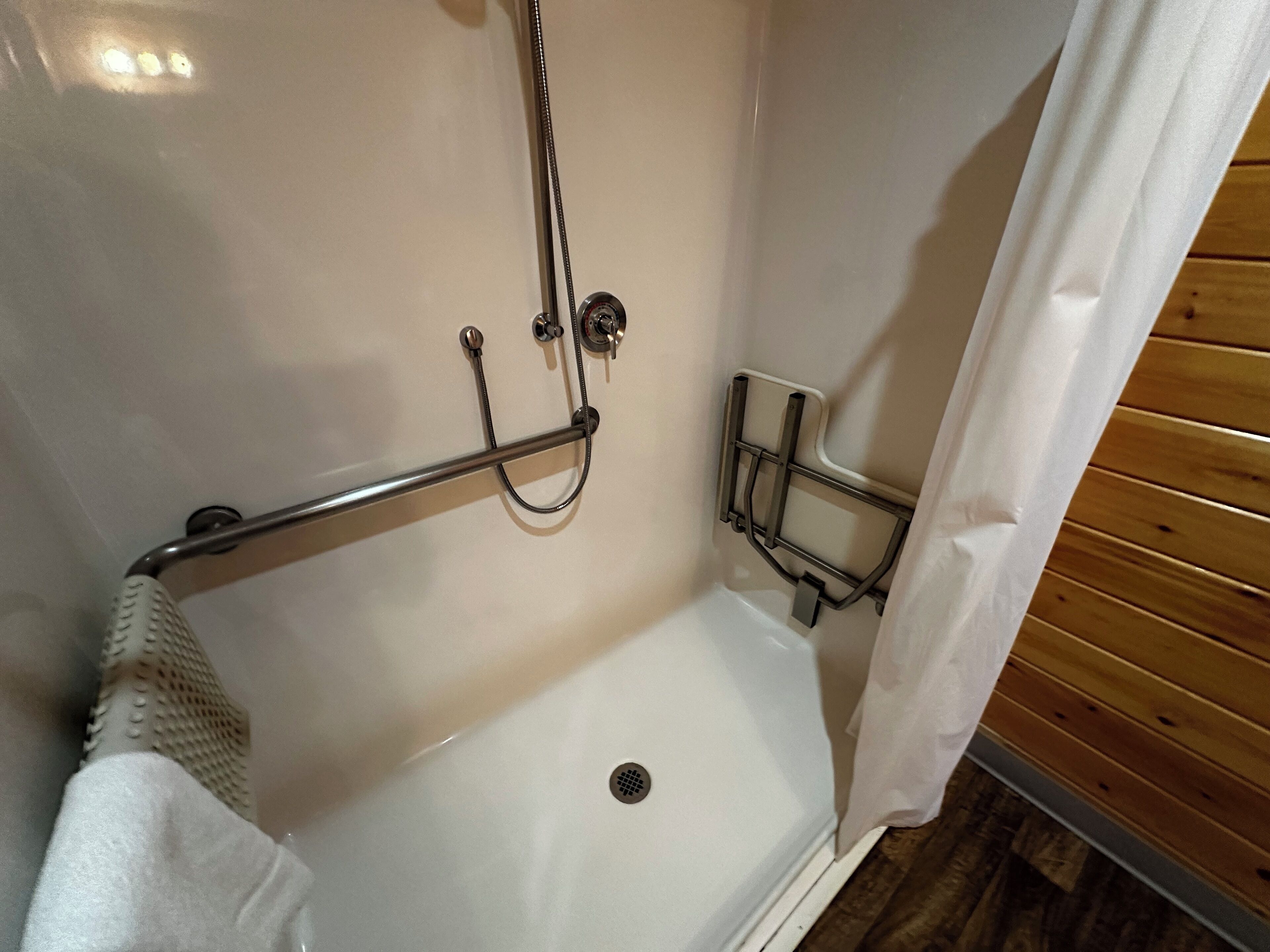 A shower area with a white bathtub, a grab bar, and a shower head.