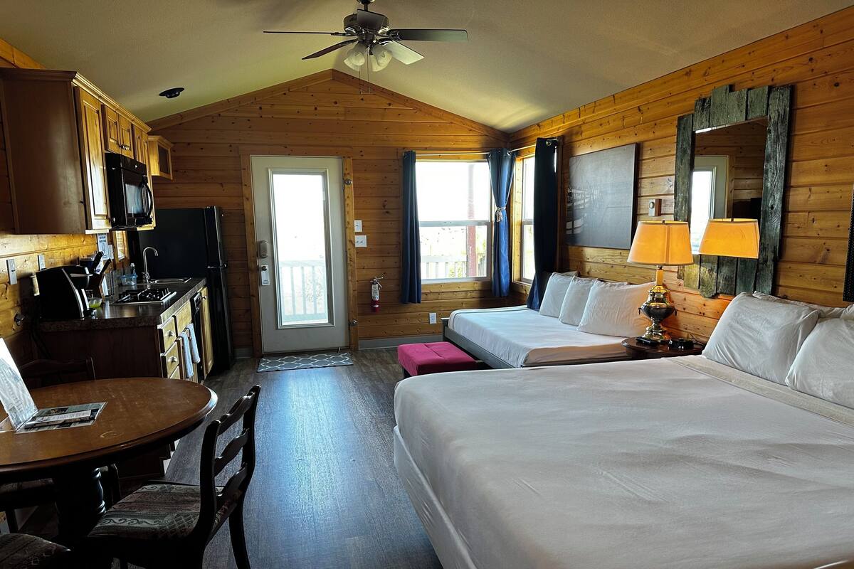 A log cabin room with a kitchenette, two beds, a dining table, and a ceiling fan.