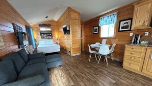 Une pièce de taille modeste, aux murs lambrissés, comprenant un canapé, un lit, une table à manger avec des chaises et un coin cuisine.