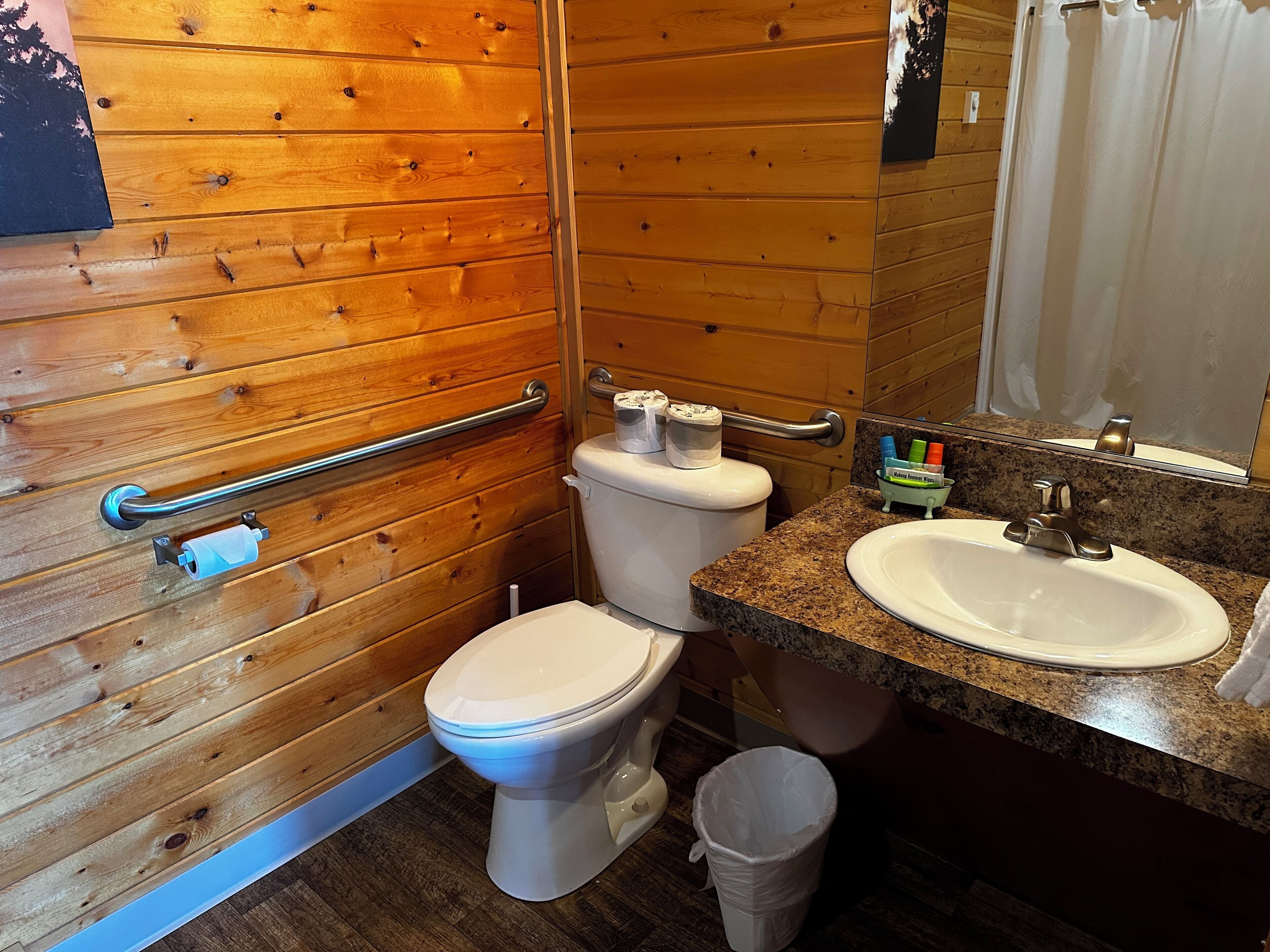 Ein Badezimmer mit Holzvertäfelung, einer weißen Toilette, einem Waschbecken und einem Mülleimer.