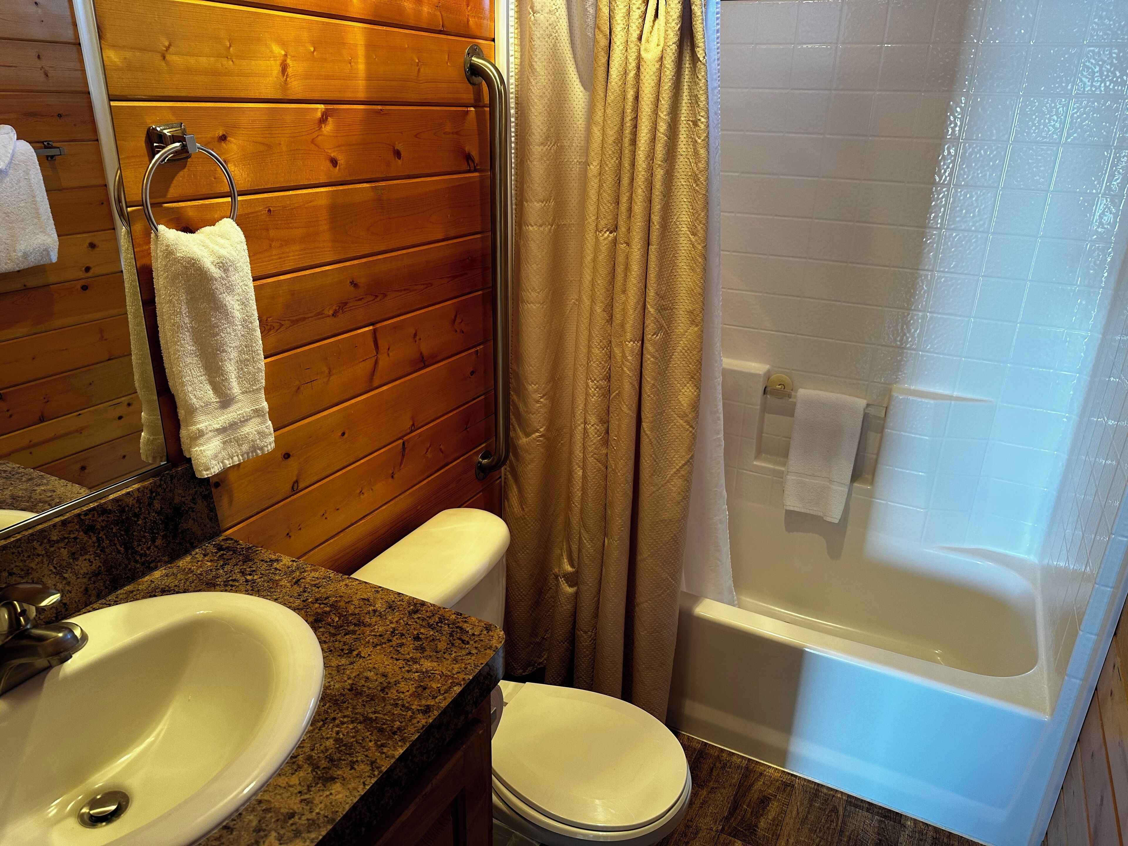 A bathroom with wooden walls, a white sink, a toilet, and a bathtub.