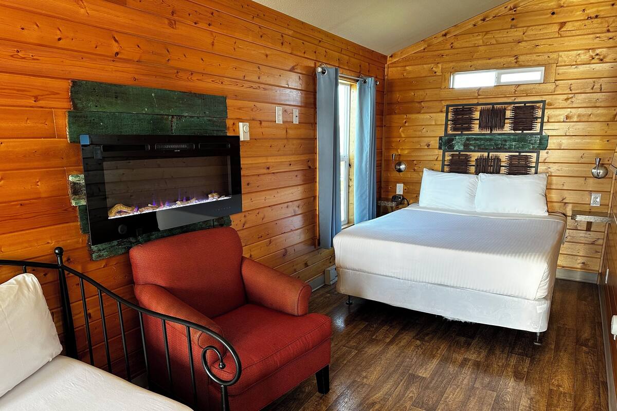 A cozy room with a bed, a red chair, a fireplace, and wooden walls.