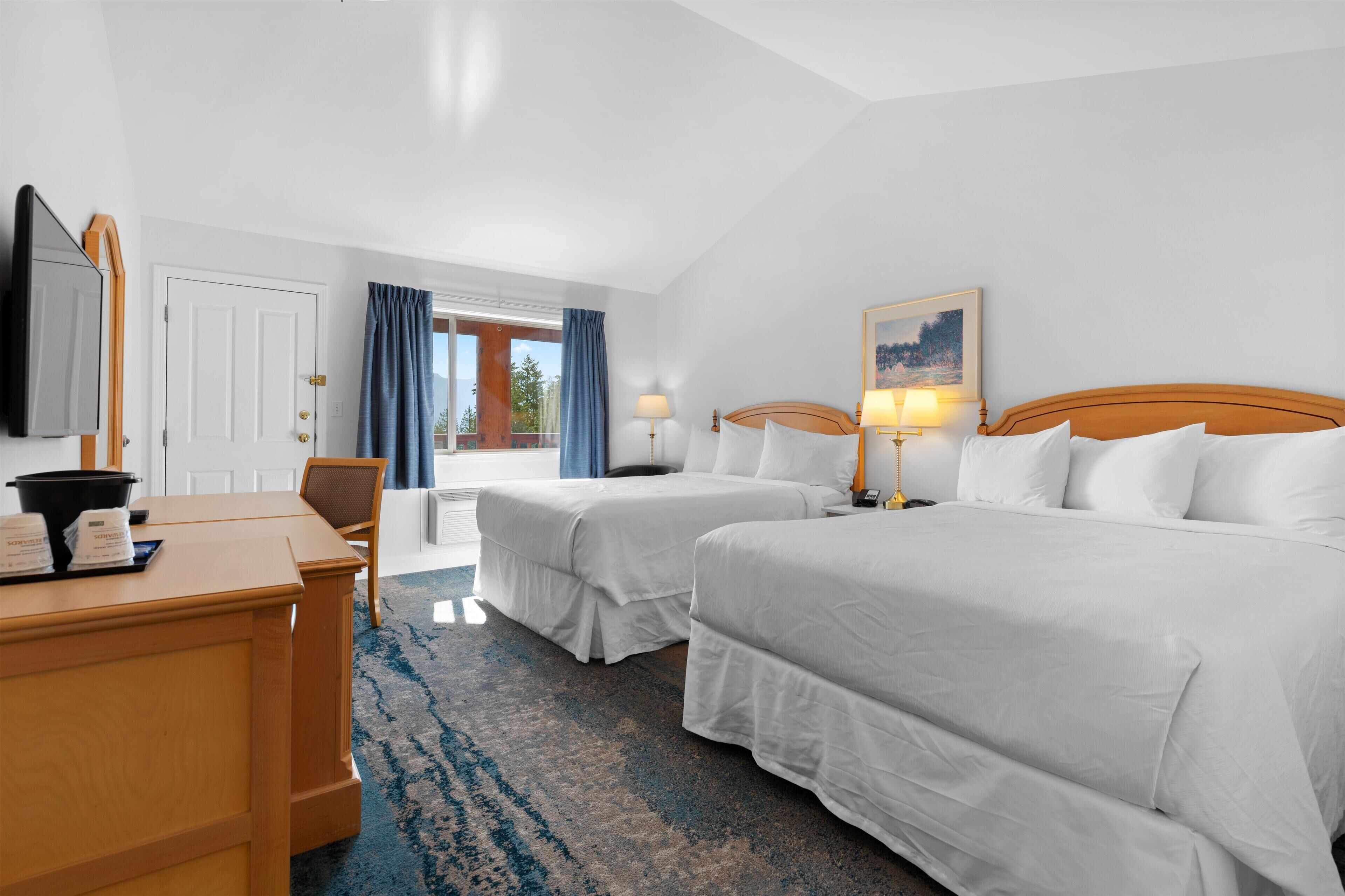 A hotel room with two beds, a desk with a mirror, a chair, and a painting on the wall.