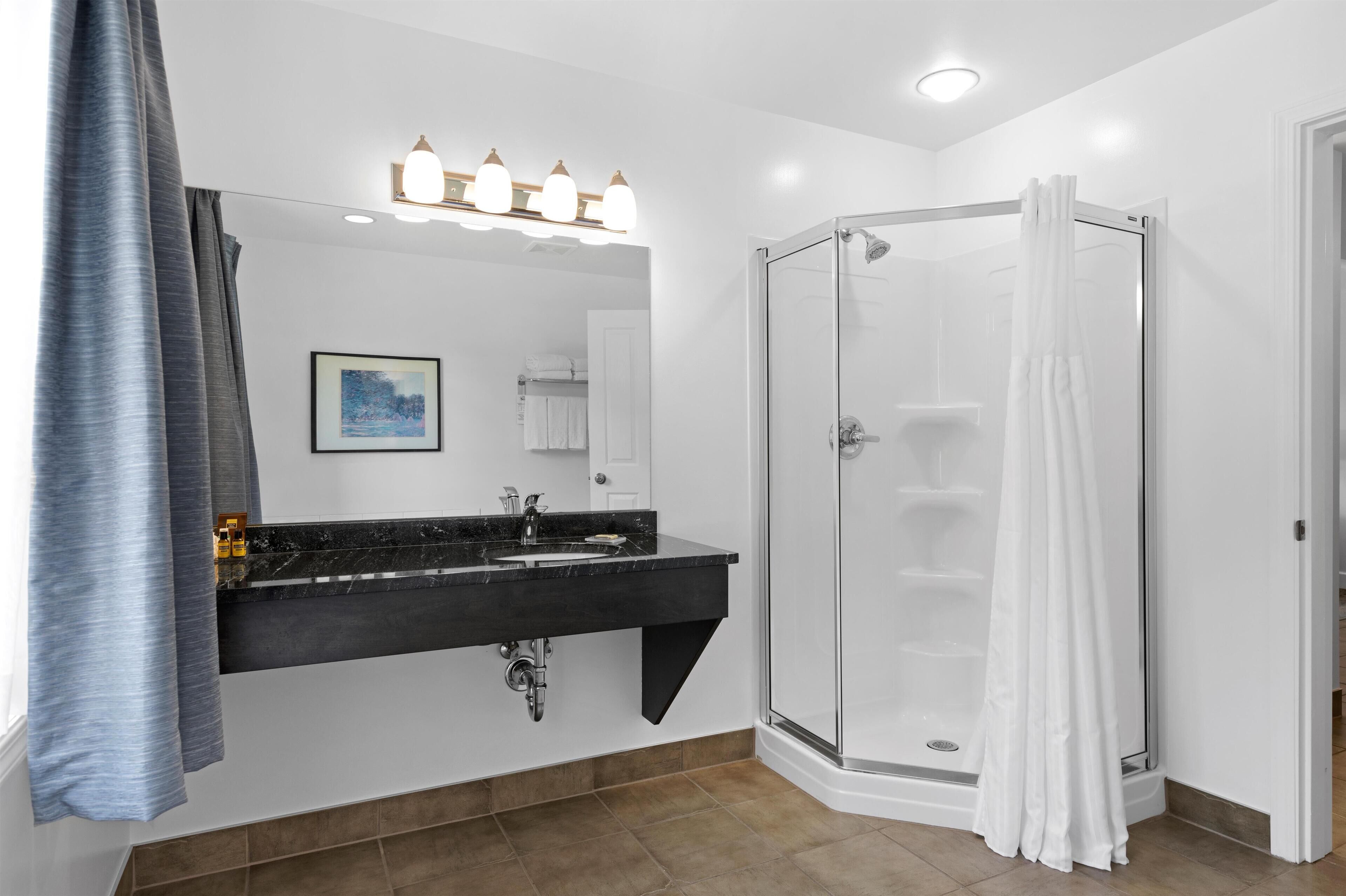Un baño con lavamanos de mármol negro, cabina de ducha de cristal y cortina de ducha blanca.