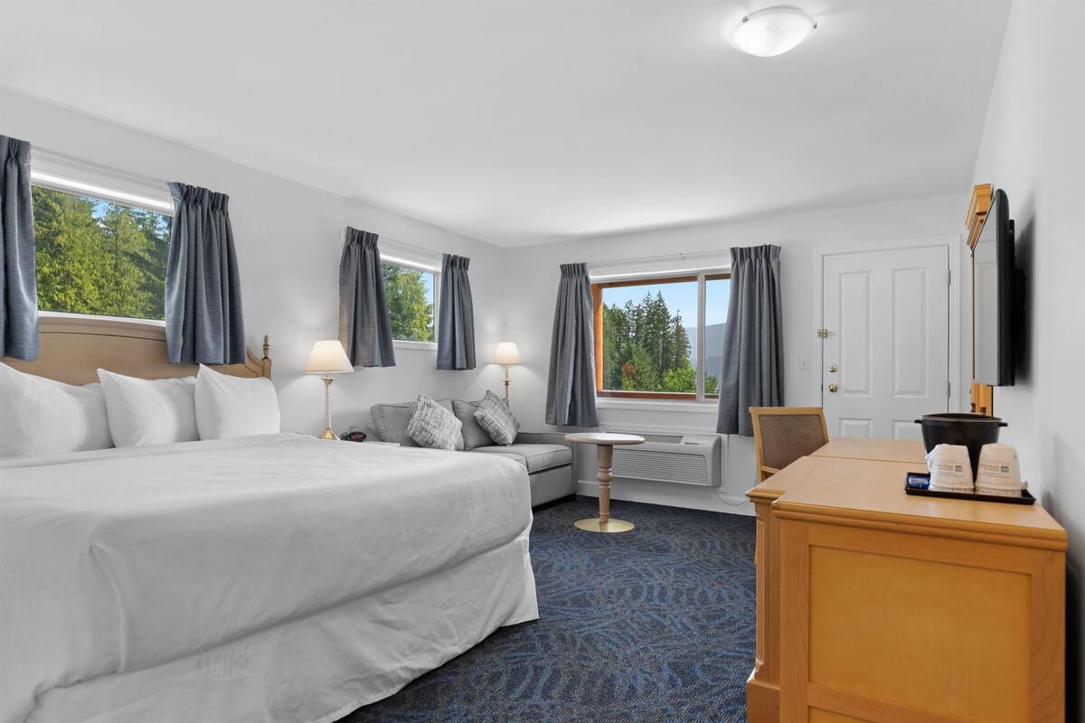 Une chambre d’hôtel avec un grand lit, un bureau, une chaise, une petite table et un téléviseur.