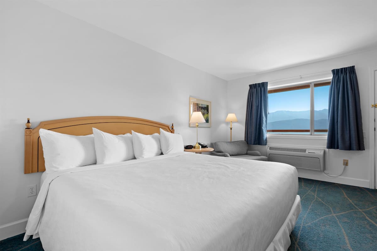 Une chambre d’hôtel avec un grand lit, un bureau avec une lampe, une chaise et une fenêtre avec des rideaux.