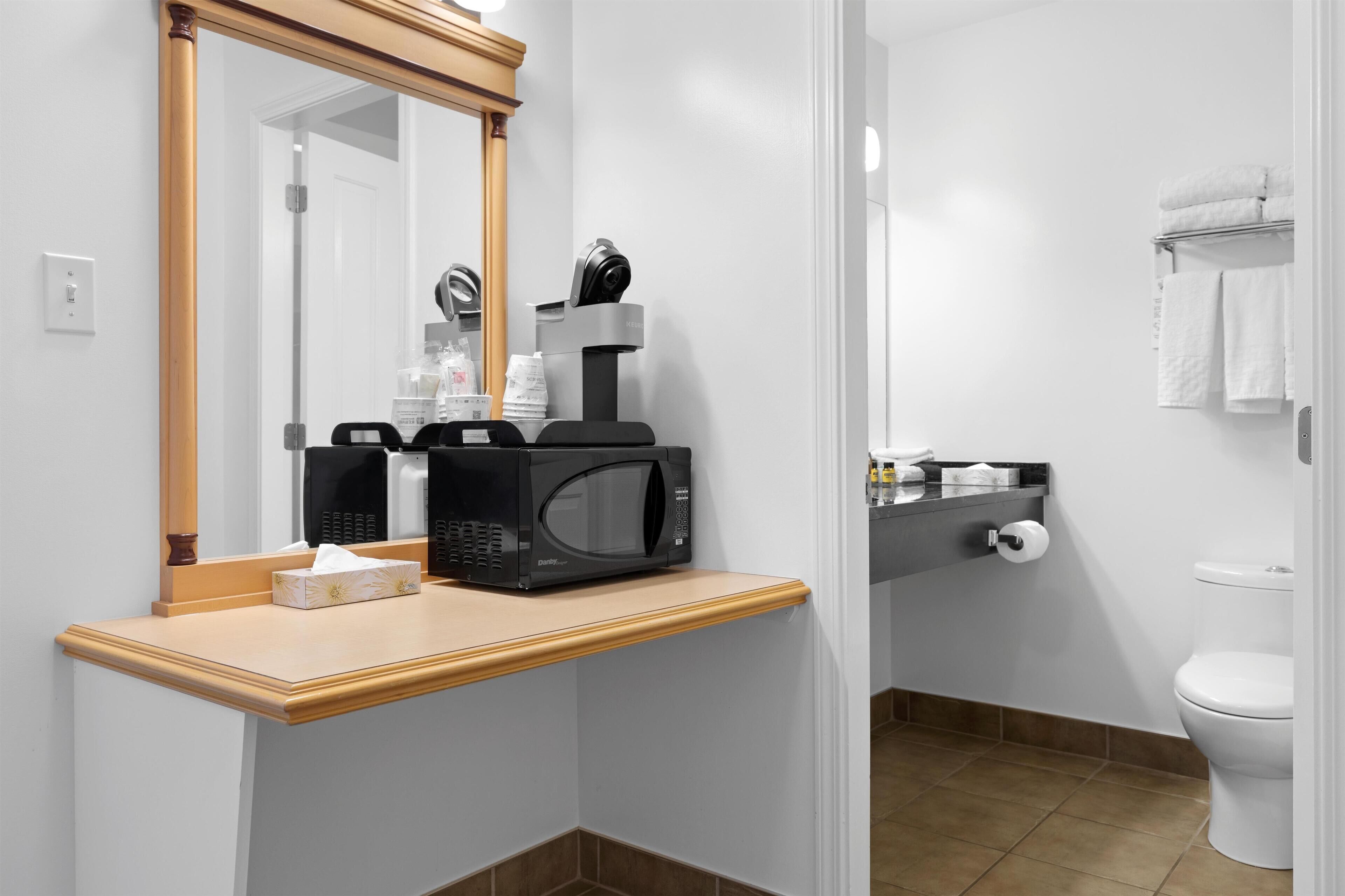 A bathroom with a microwave, coffee maker, and toiletries on a countertop.
