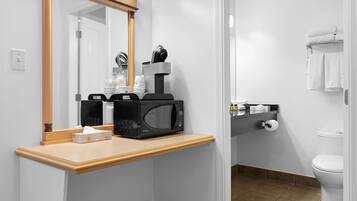 A bathroom with a microwave, coffee maker, and toiletries on a countertop.