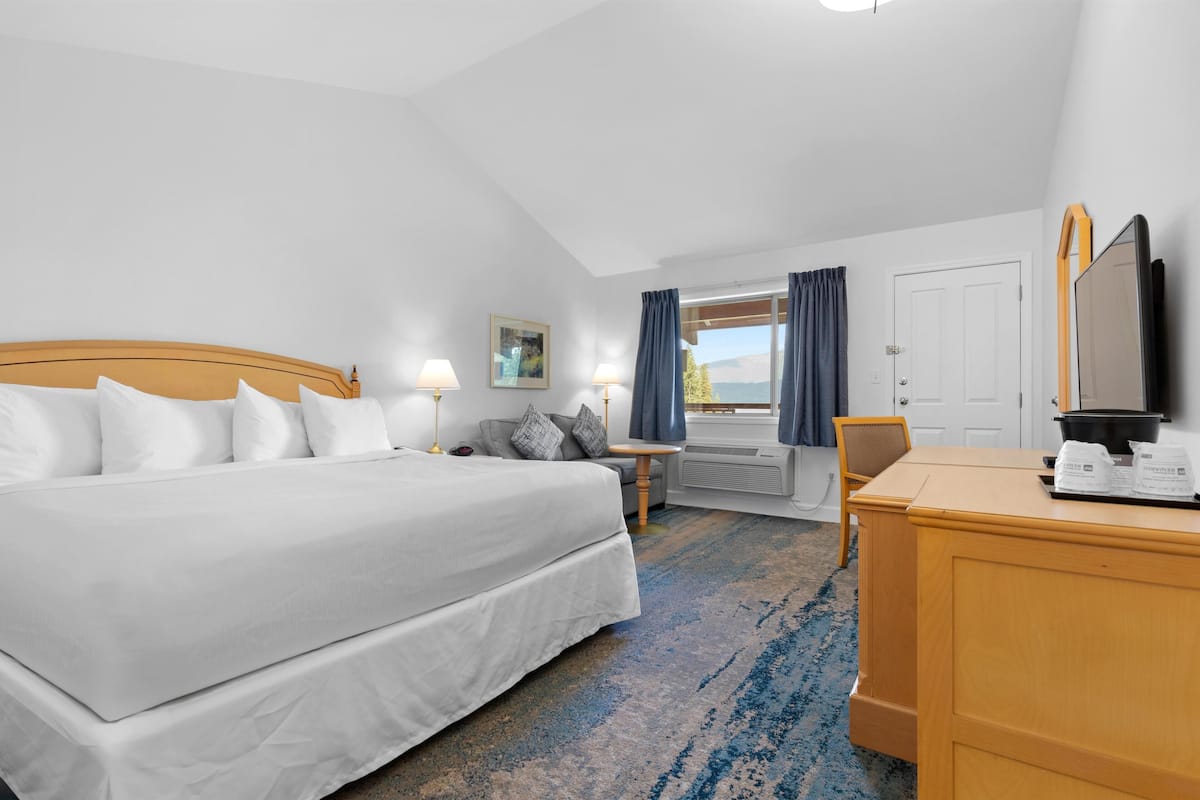 Une chambre d’hôtel avec un grand lit, un bureau, une chaise, une petite table, un téléviseur et une fenêtre avec des rideaux.