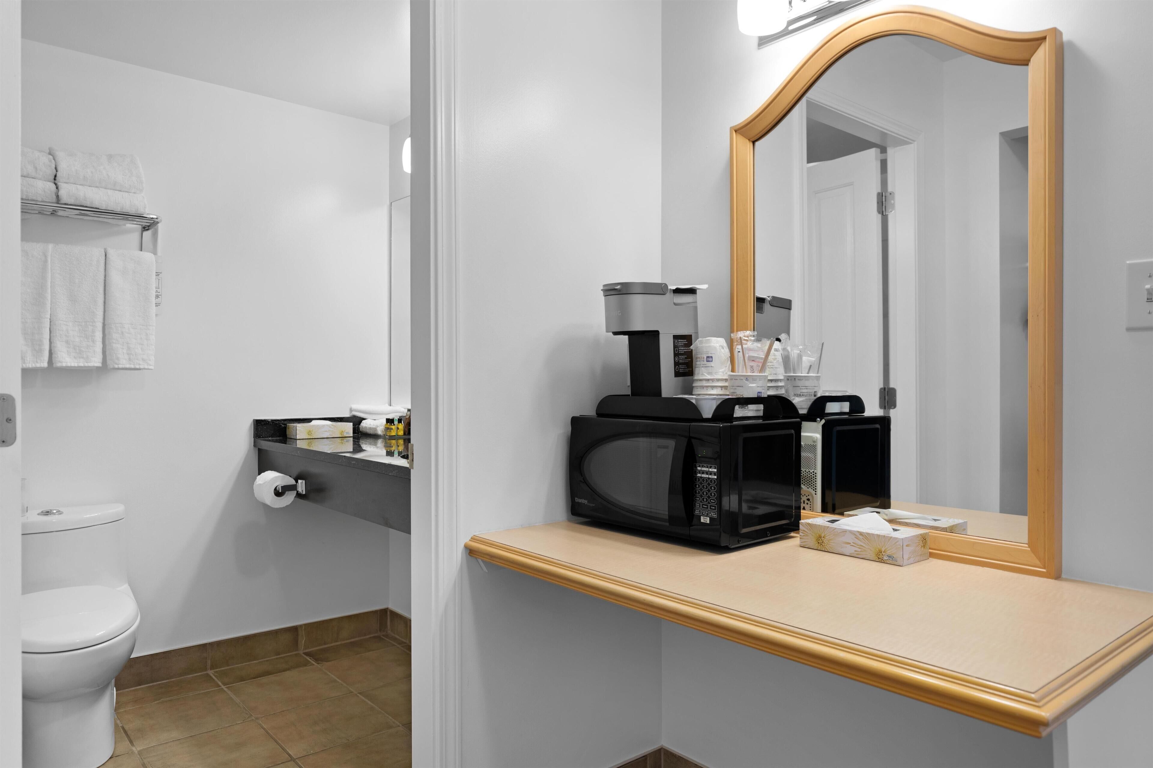 Un baño con inodoro, perchero para toallas, lavabo con espejo y cafetera.