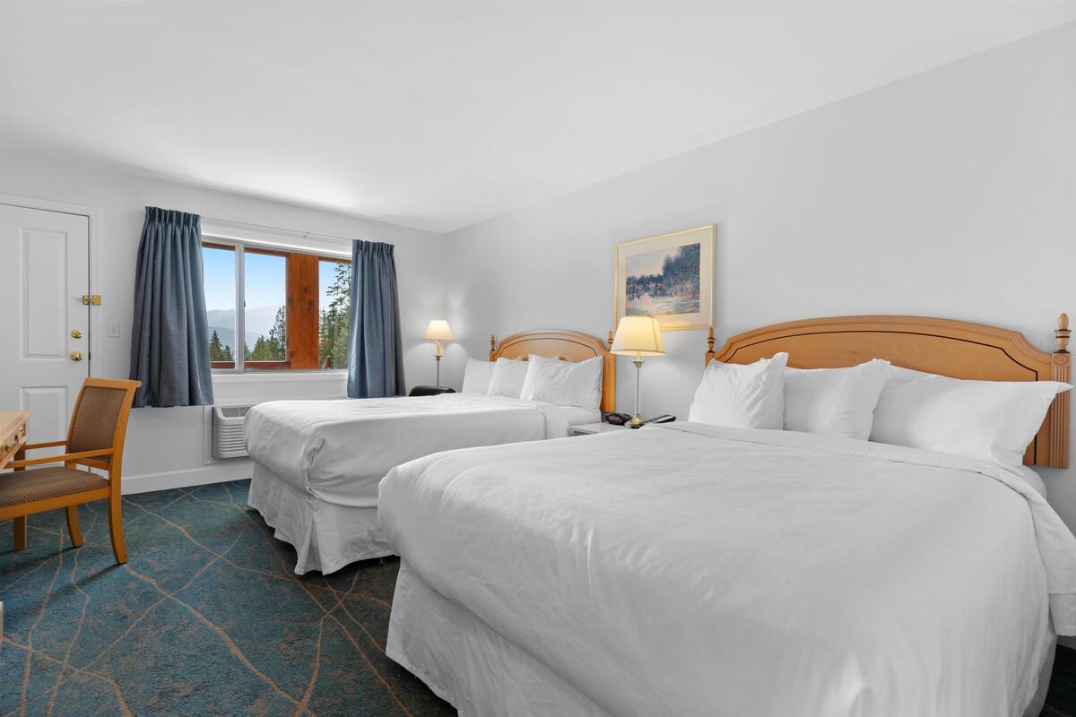 Une chambre d’hôtel avec deux lits, une chaise, un bureau, une fenêtre avec des rideaux et un tableau au mur.