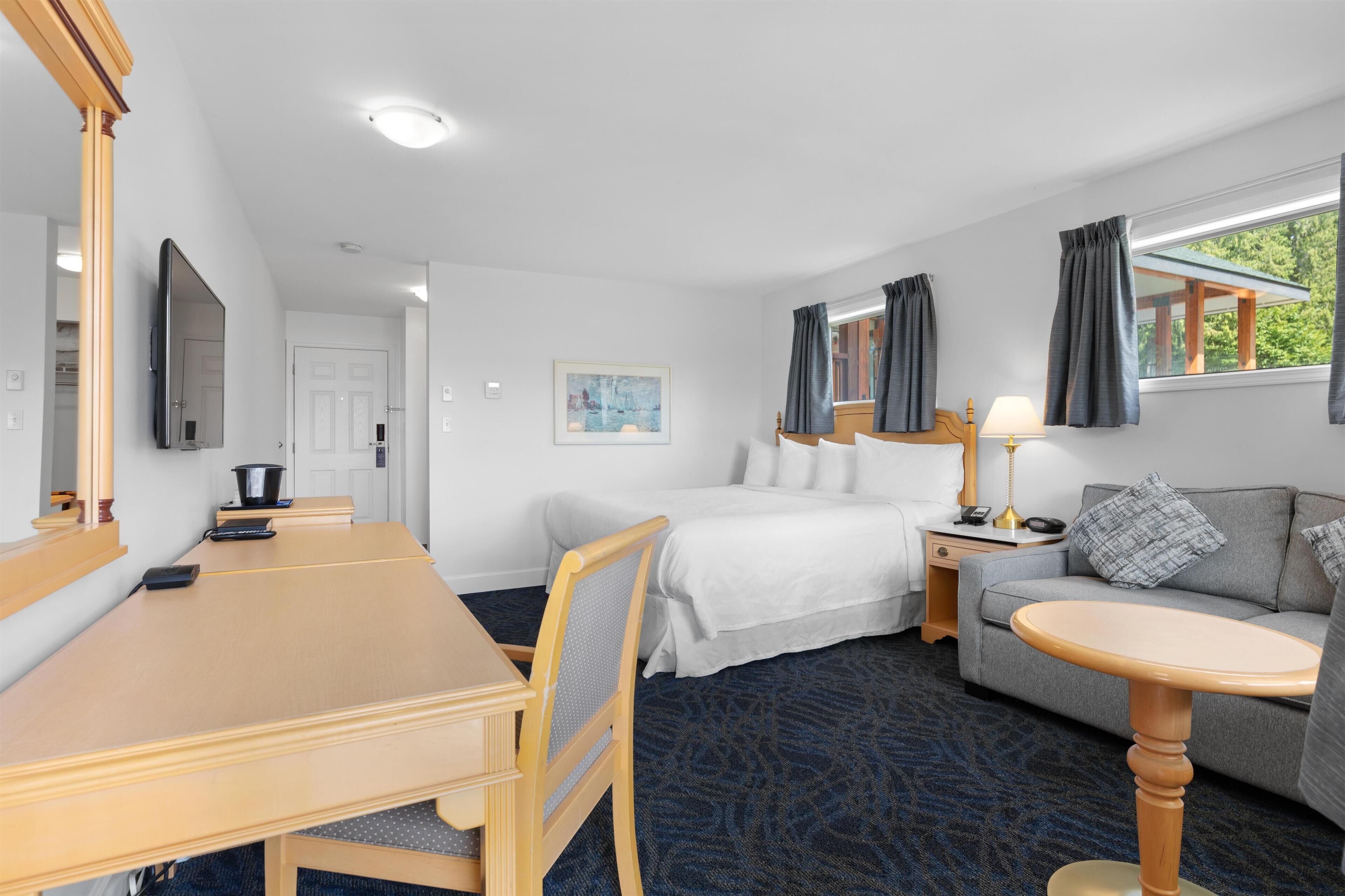 A hotel room with a bed, a sofa, a dining table, and a TV.
