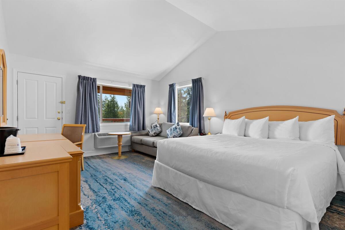 Une chambre d’hôtel avec un grand lit, un bureau, une chaise, un canapé et une fenêtre avec des rideaux.
