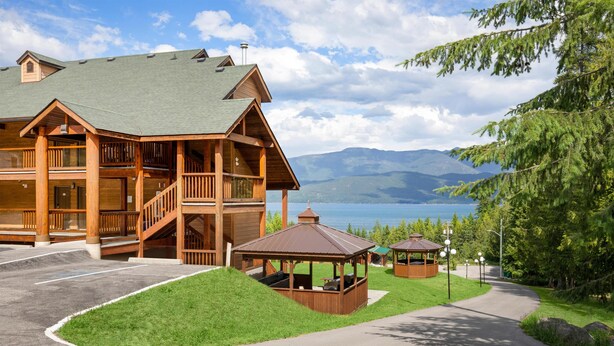 Un grand chalet en bois doté de nombreux balcons et d’un belvédère, situé dans un cadre magnifique avec des montagnes et un lac en toile de fond.