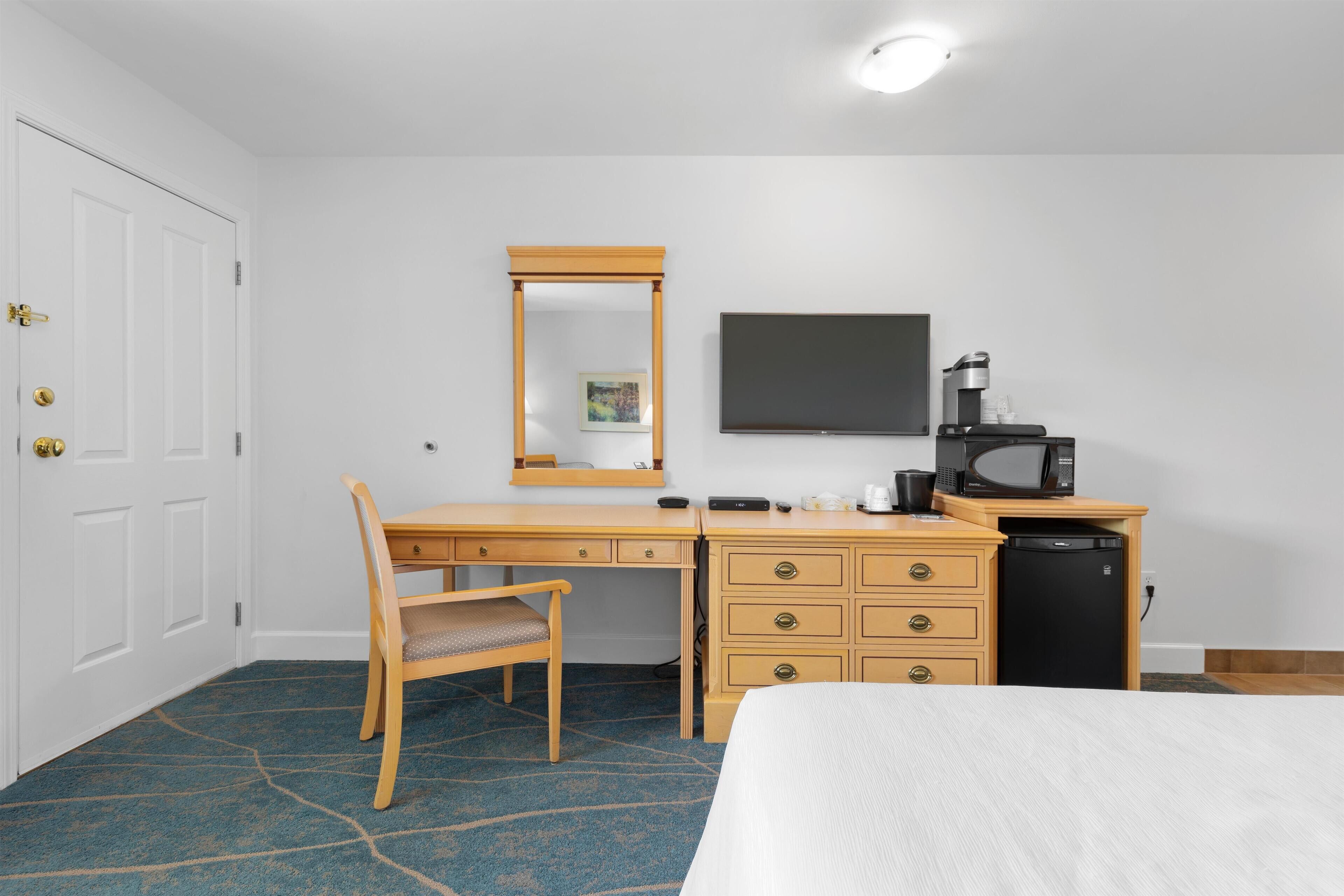 A hotel room with a bed, a desk with a chair, a dresser, a television, and a microwave.