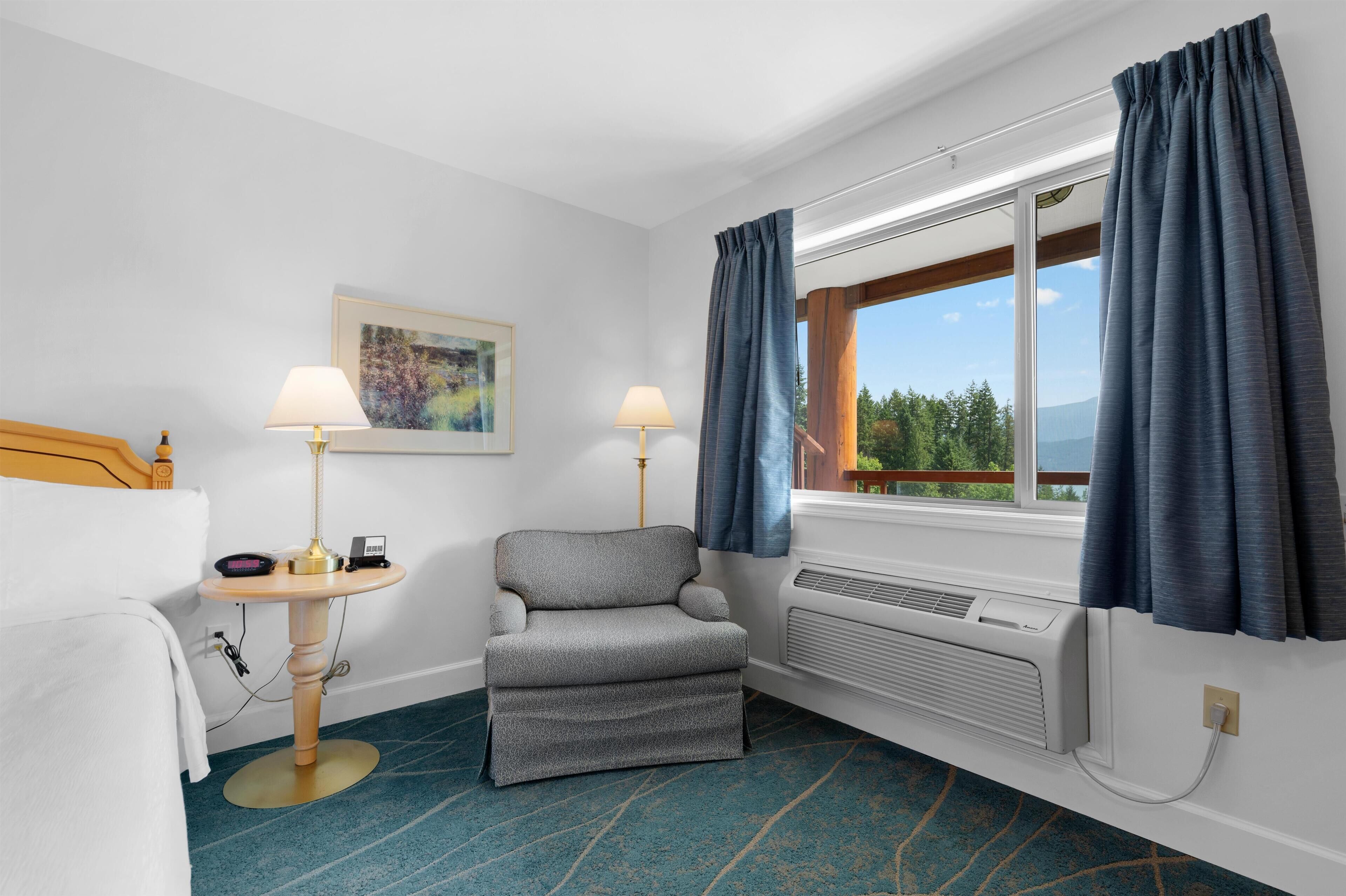 A hotel room with a bed, two bedside lamps, a chair, a window with curtains, a painting on the wall, and a view of the outdoors.