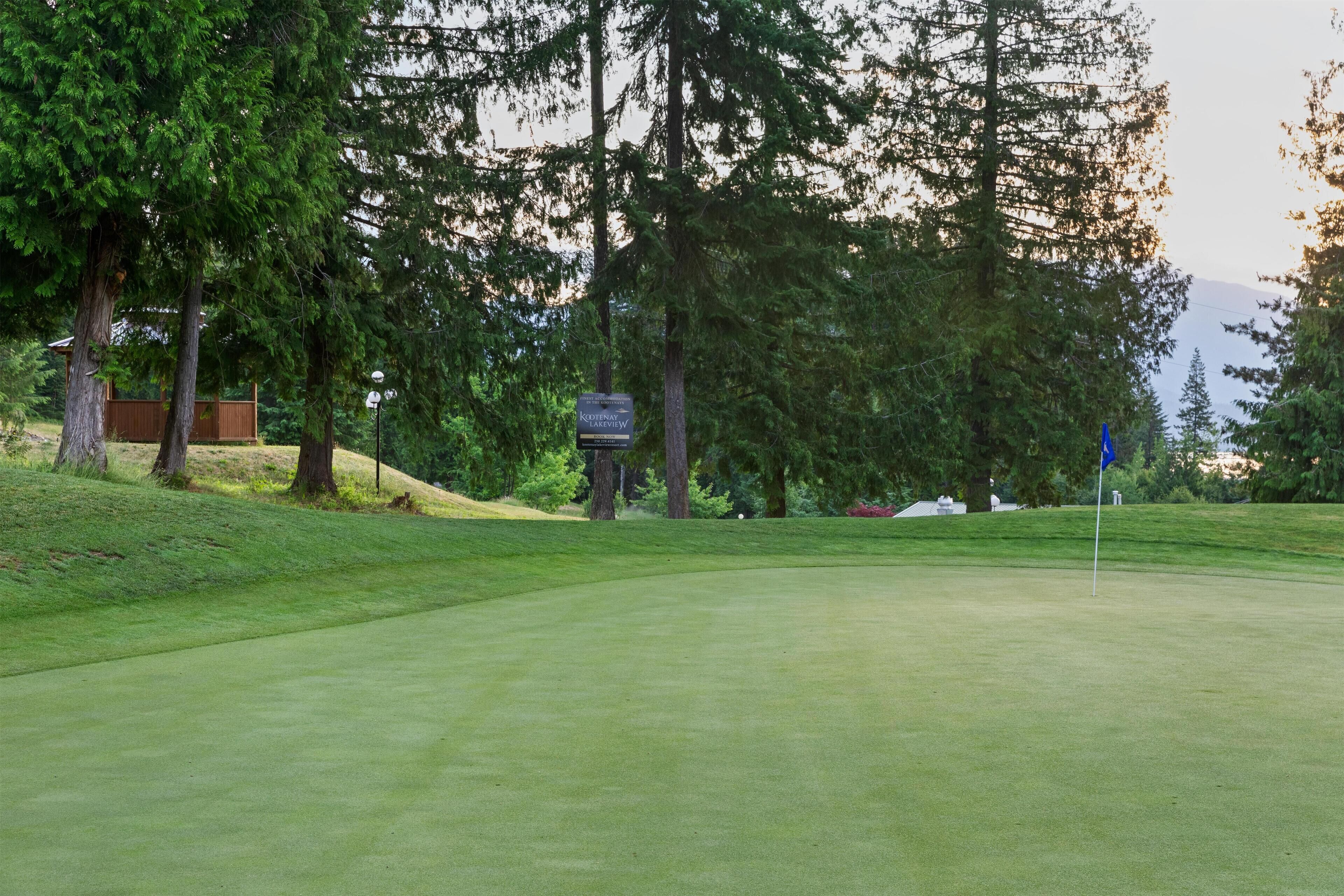 Un parcours de golf avec un mât de drapeau, des arbres et un panneau indicateur.