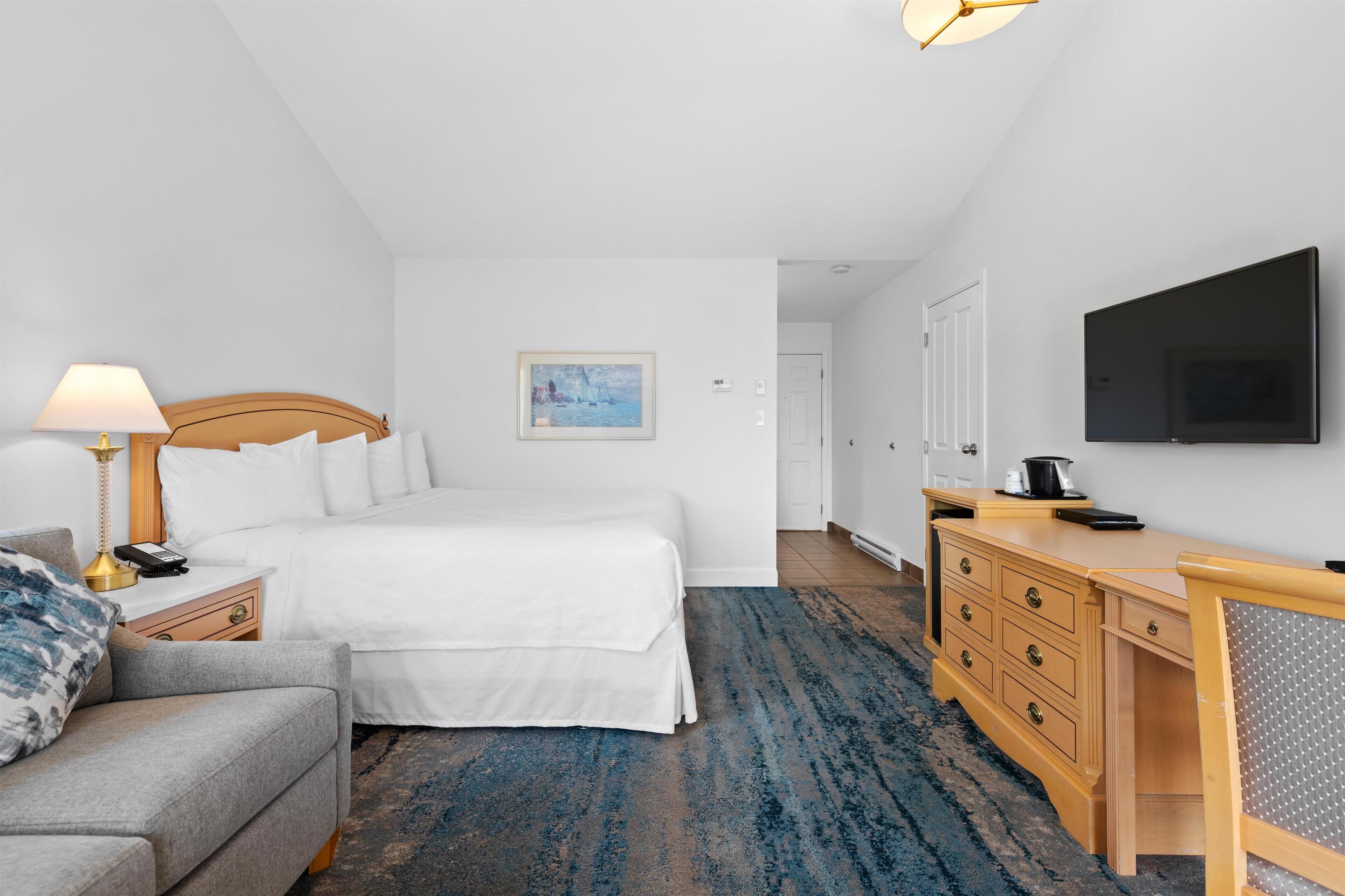 A hotel room with a bed, a desk, a television, a lamp, and a painting on the wall.